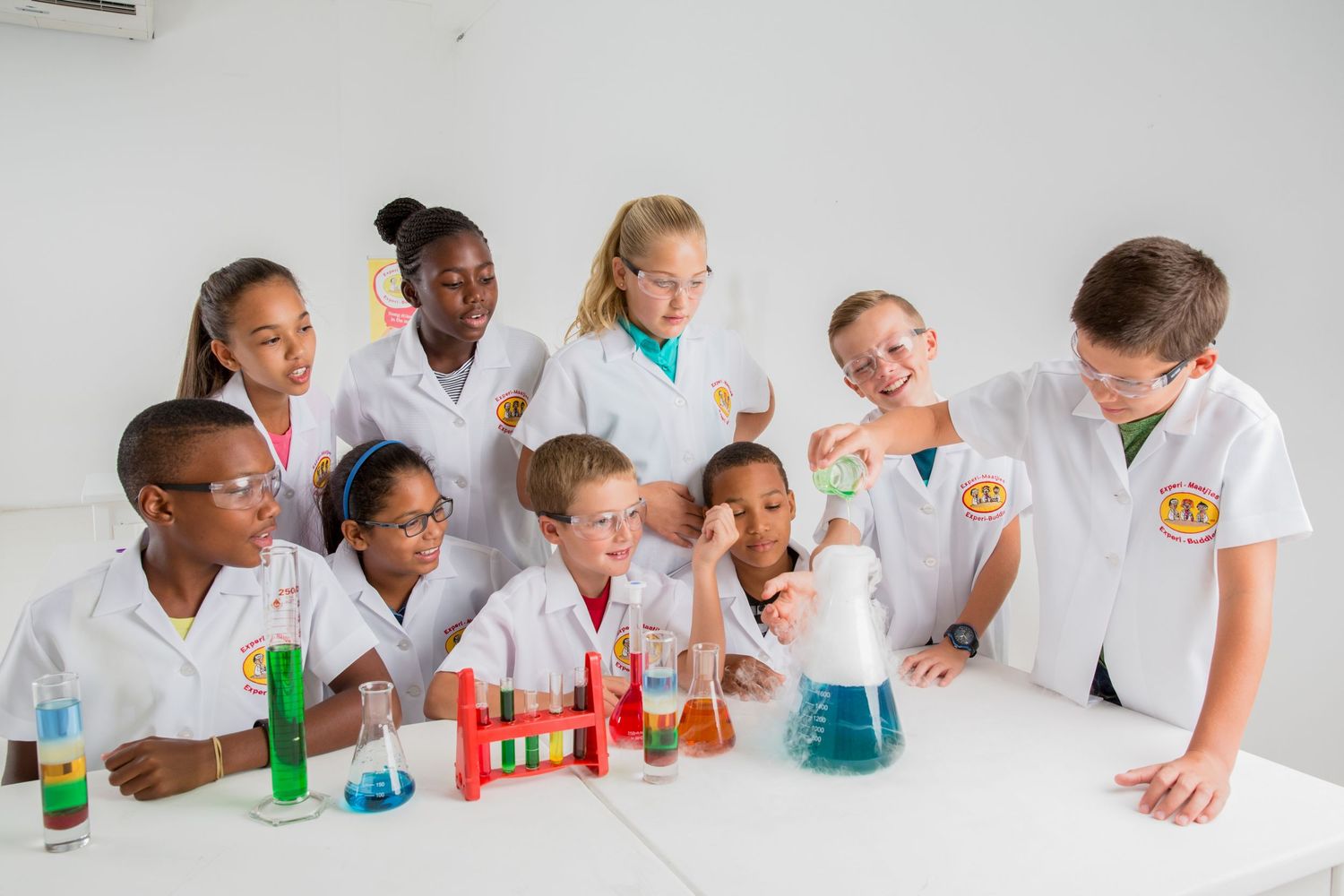 Excited students gather around a table with colorful chemistry experiments and lab equipment.