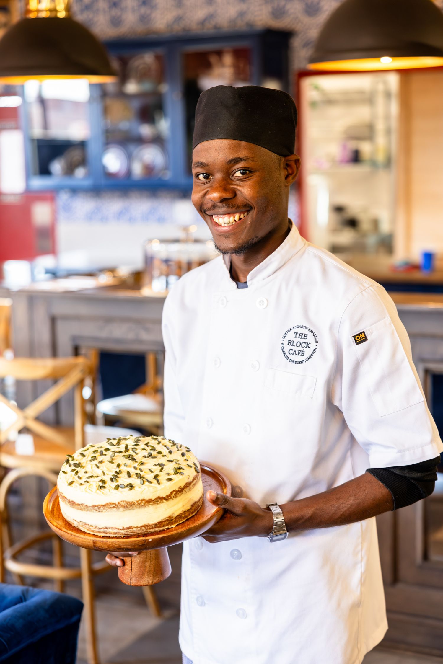 Chef displaying an artfully decorated cake with nuts and cream in a restaurant setting.