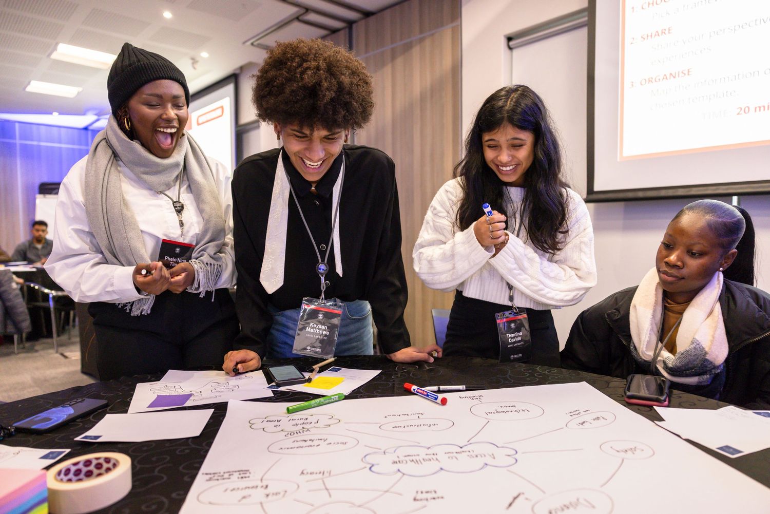 Workshop participants engaging in group activities at tables in a bright room.