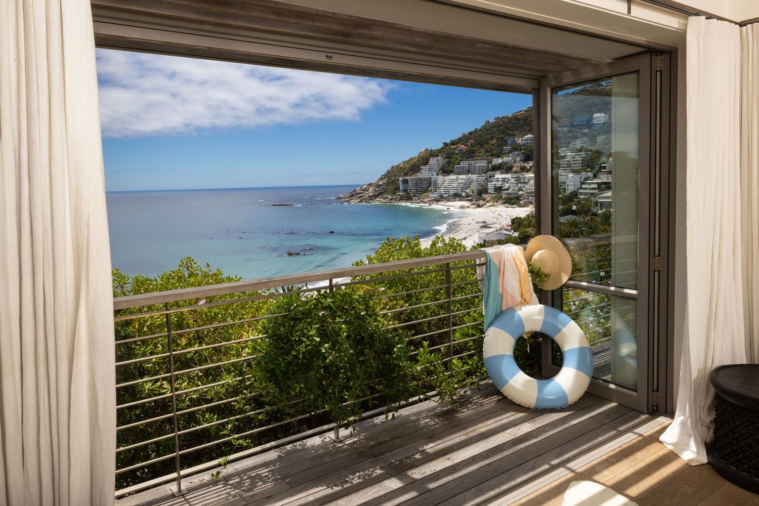 A modern coastal villa with panoramic ocean views through large windows and white curtains framing the scenic landscape.