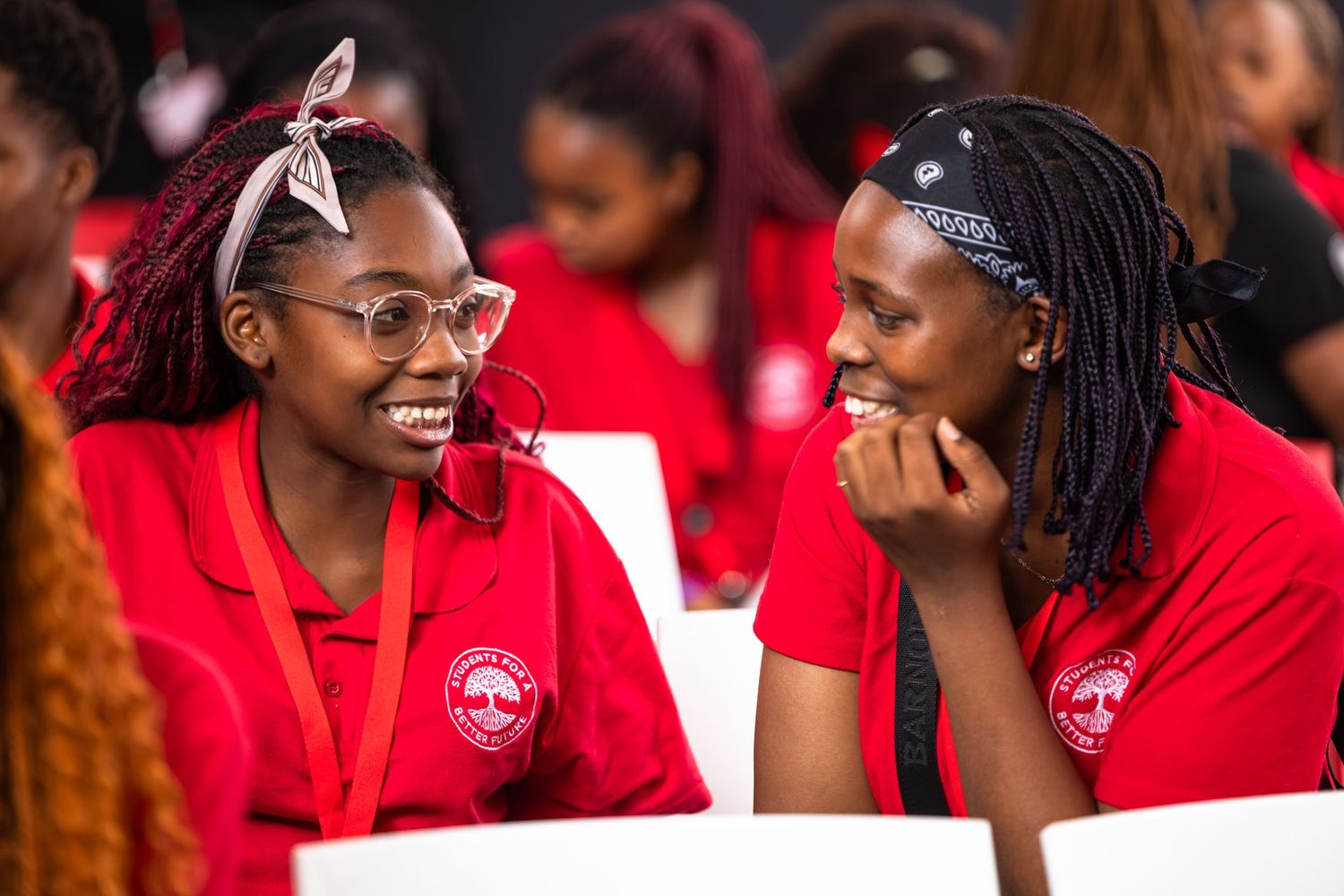 Conference participants in red uniforms share animated conversation during event.