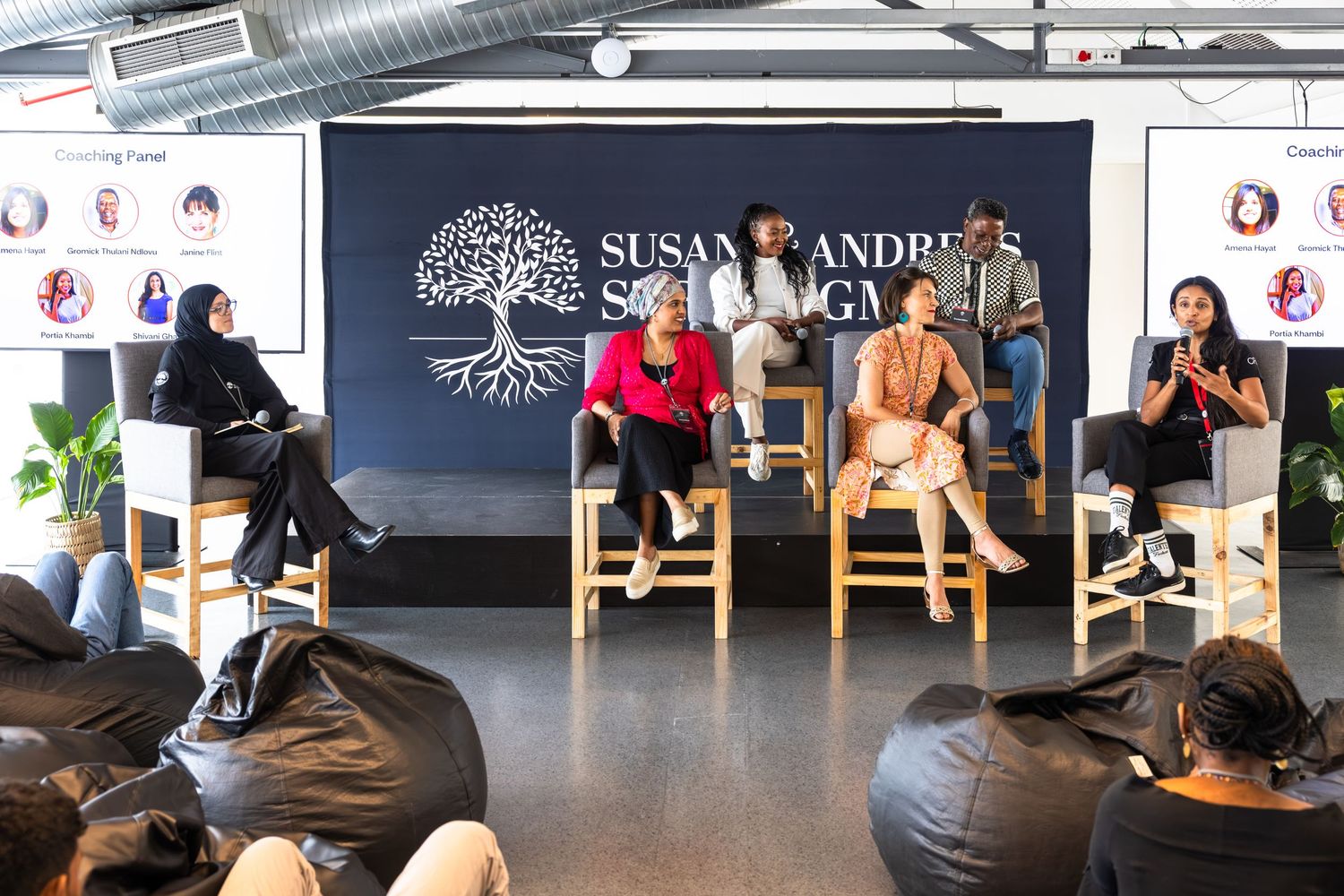 Panel discussion setup with speakers seated on high chairs in front of branded backdrop at corporate event.