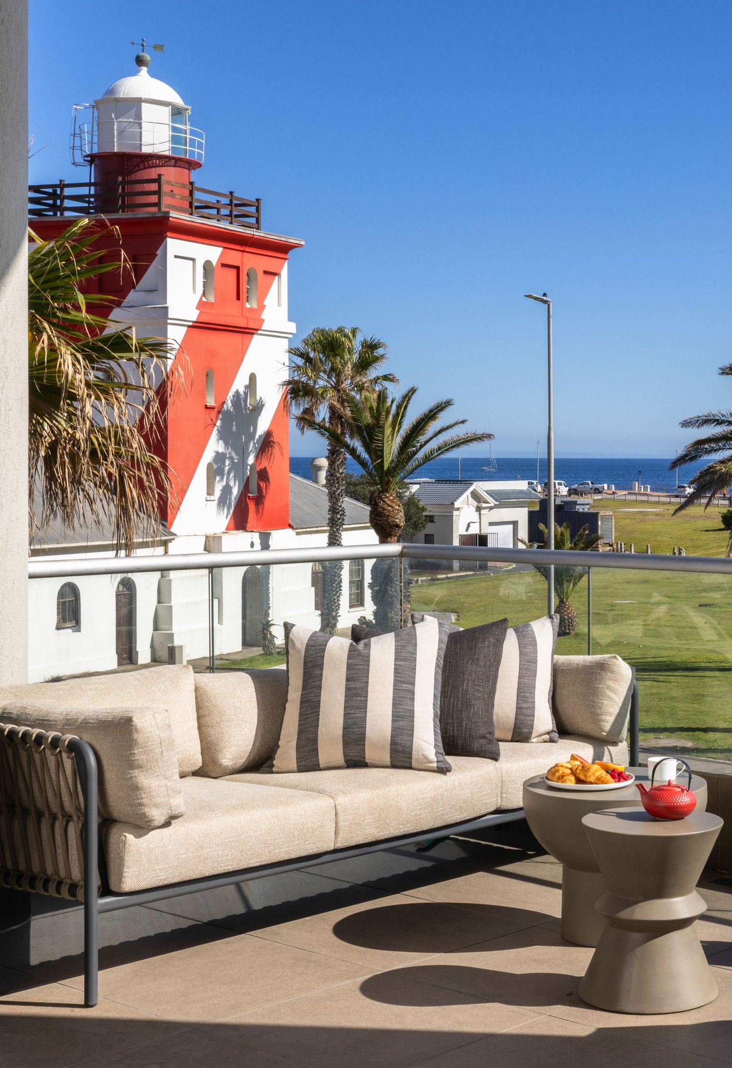 Outdoor seating area with beige cushioned furniture overlooking a lighthouse and ocean view.