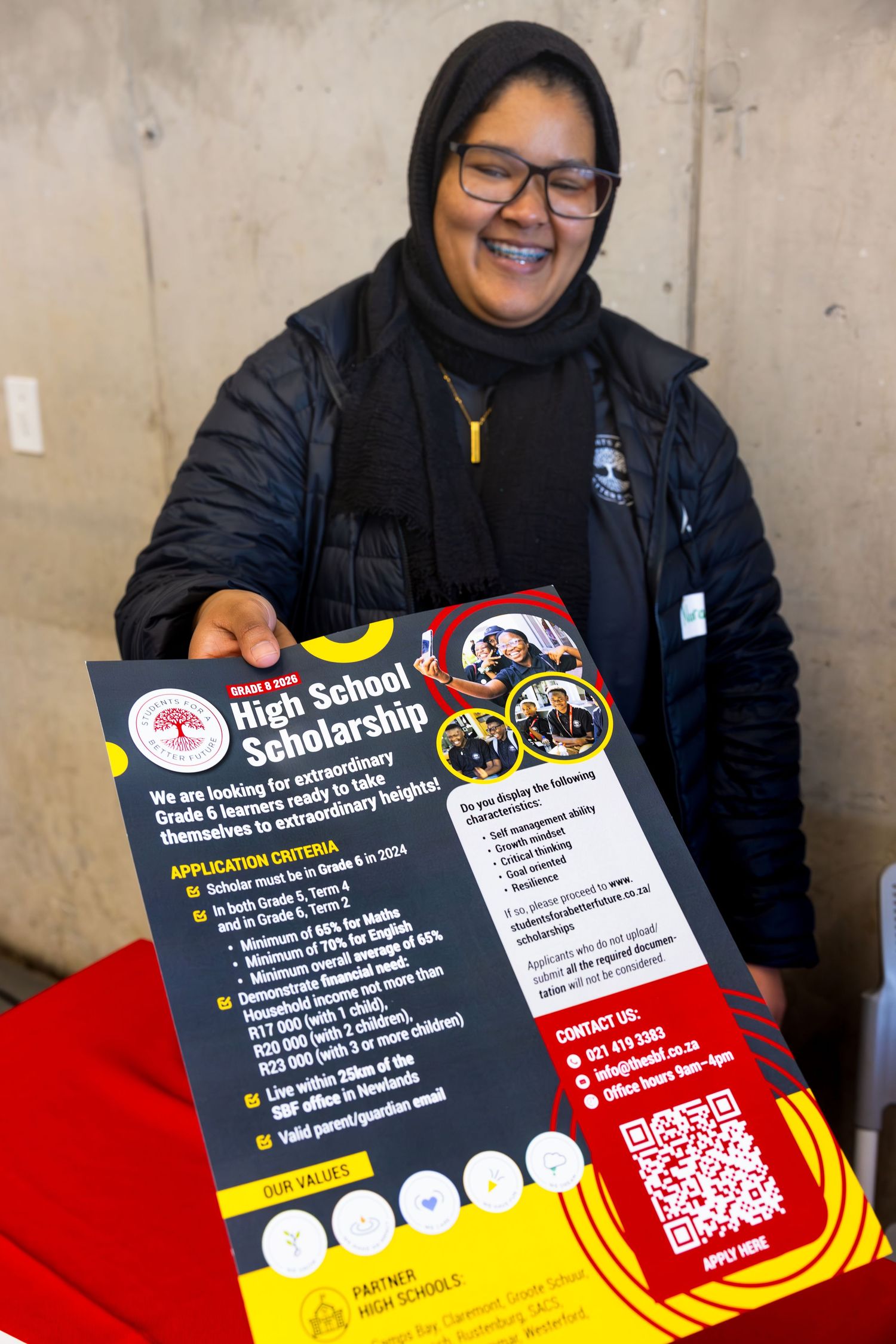 Person displaying a high school scholarship information flyer with QR code.