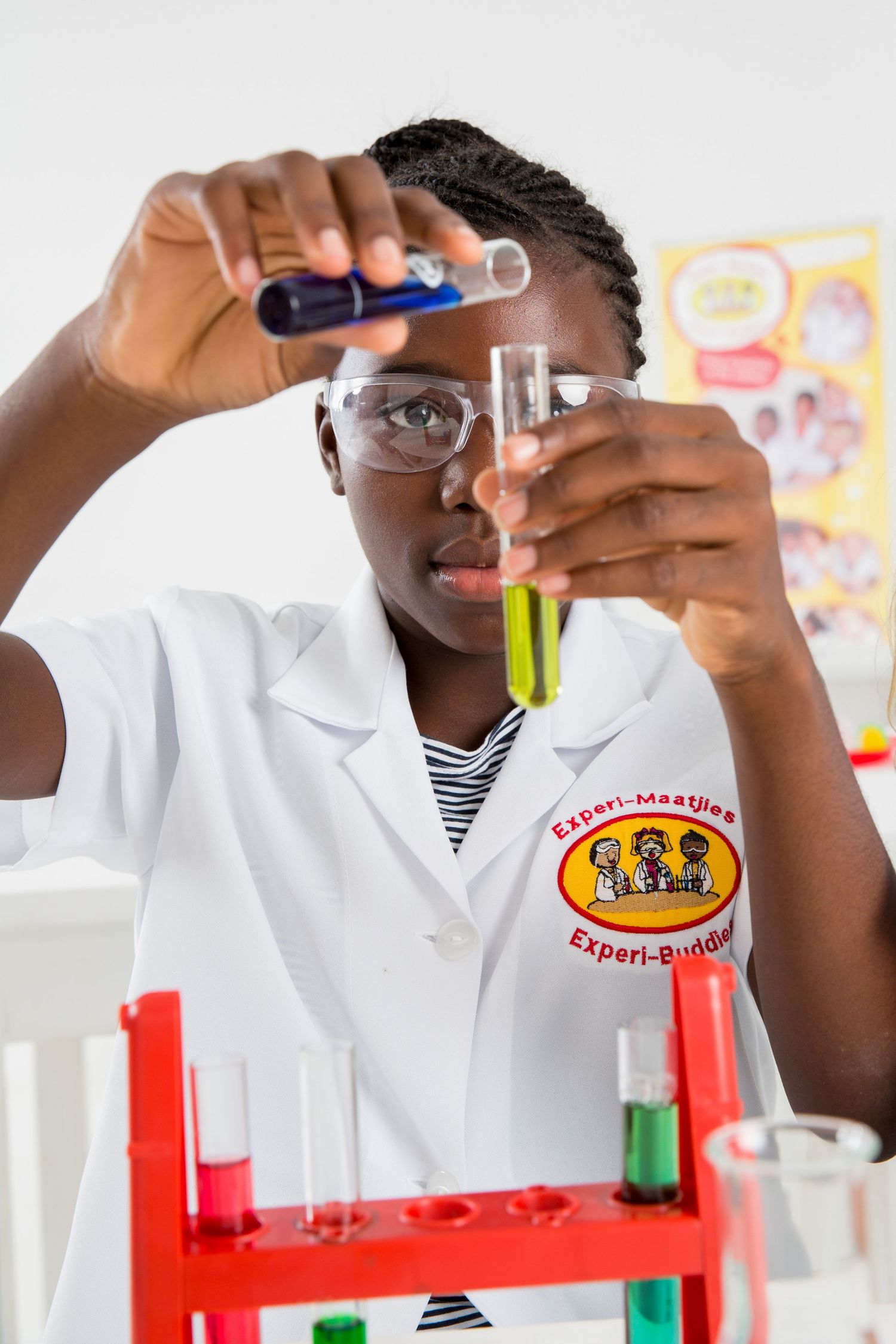 Student in lab coat and safety glasses performs liquid experiment with colorful test tubes.