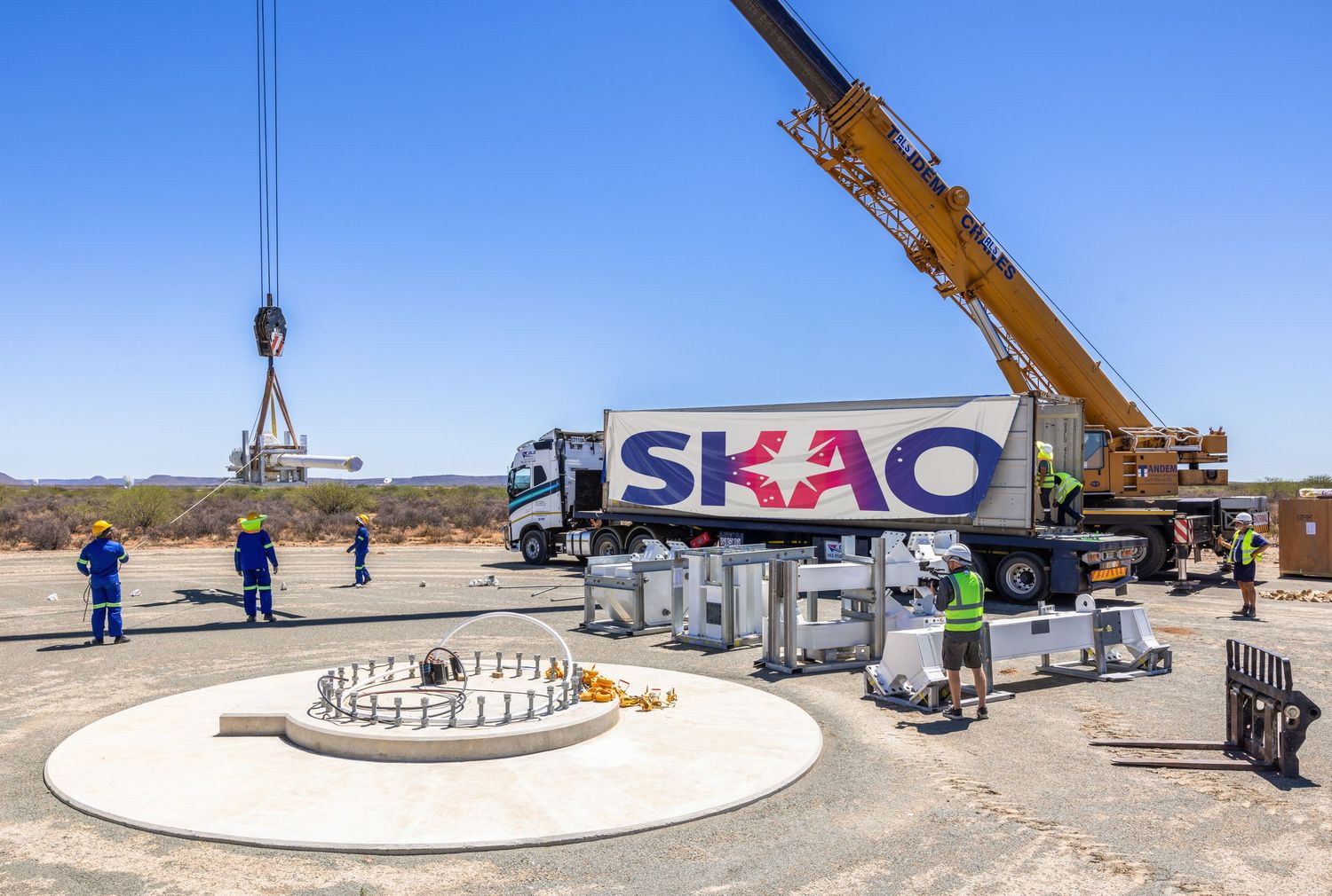 Industrial crane operations around large white cylindrical structure in desert setting.