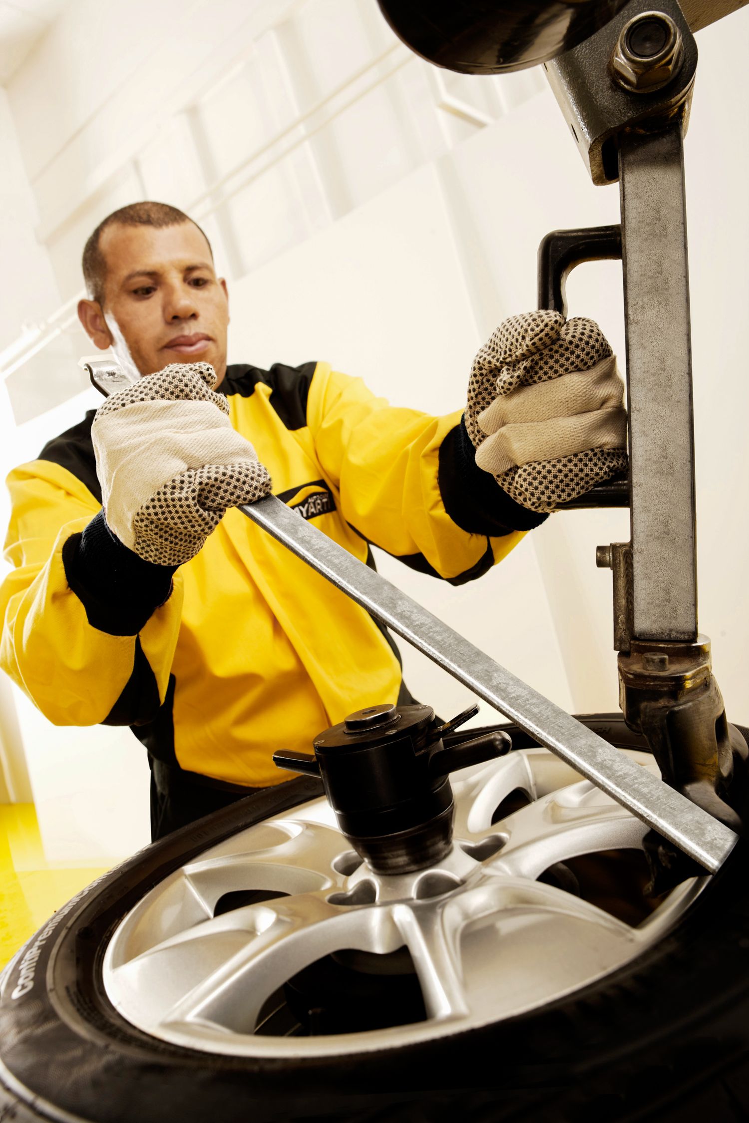 Auto mechanic in yellow uniform servicing wheel and tire assembly.