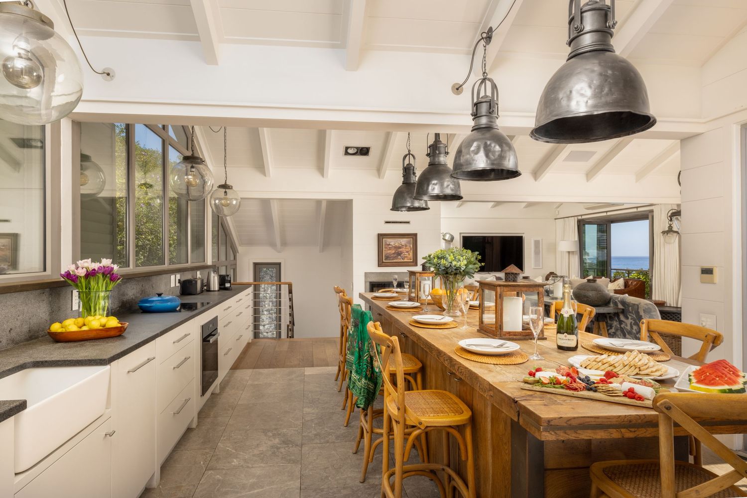 Bright kitchen interior with rustic wooden dining table, white cabinets and industrial pendant lighting.