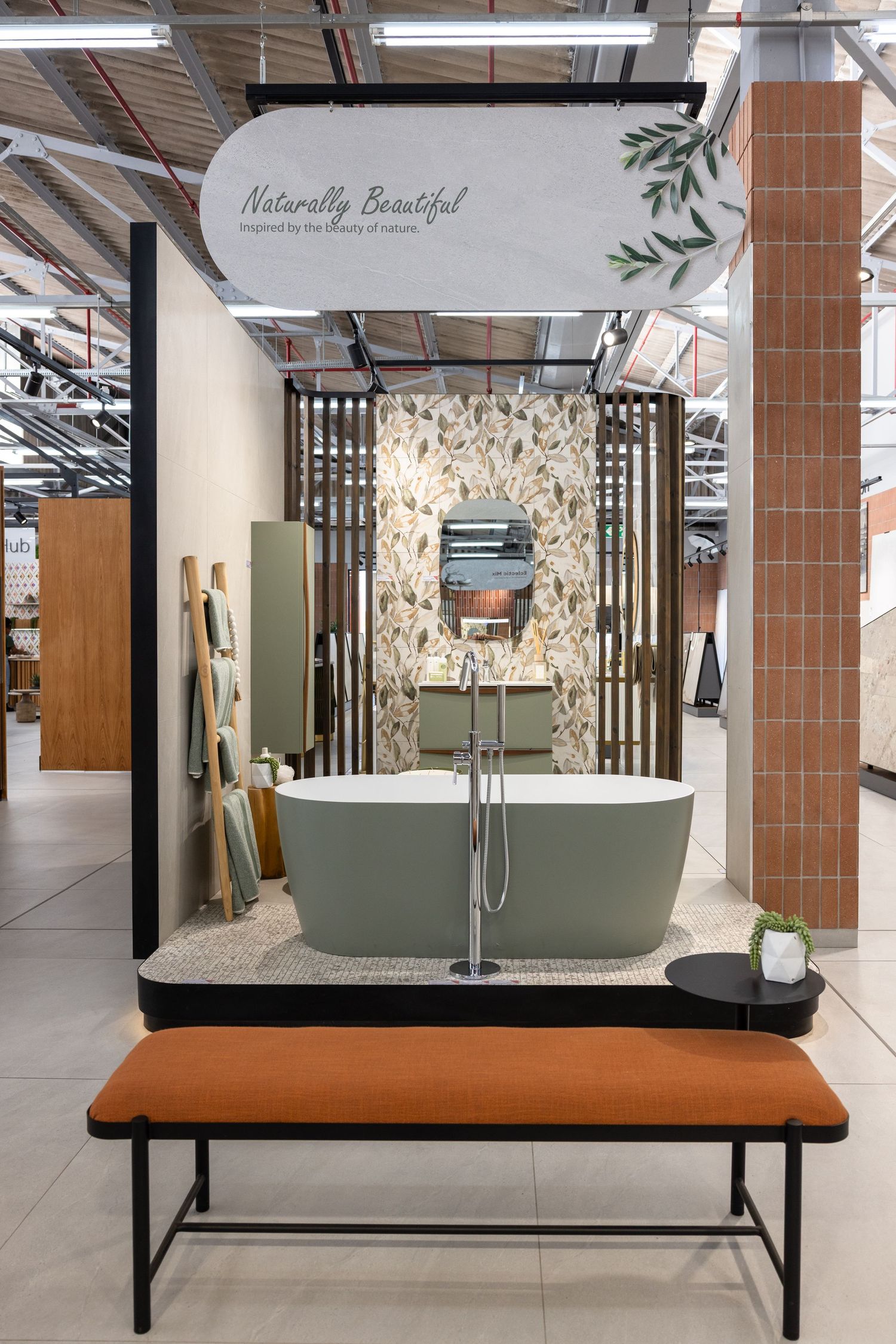 Modern bathroom display featuring a freestanding sage green bathtub against a textured wall with 'Naturally Beautiful' signage.
