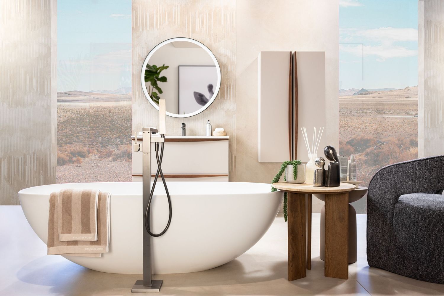 Modern bathroom with freestanding oval tub, round mirror, and desert view through large windows.