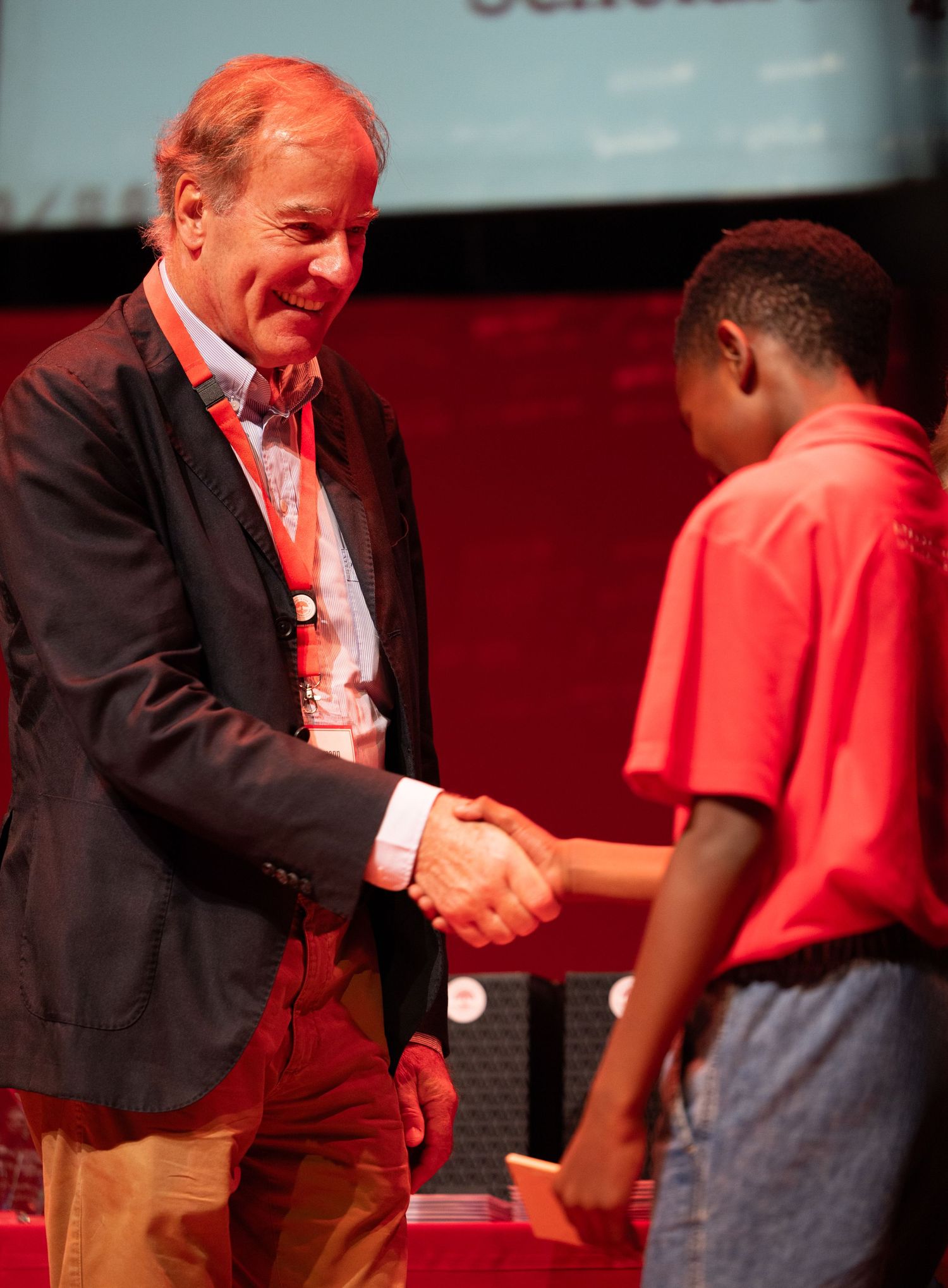 Professional handshake exchange on stage during formal ceremony with red lighting.