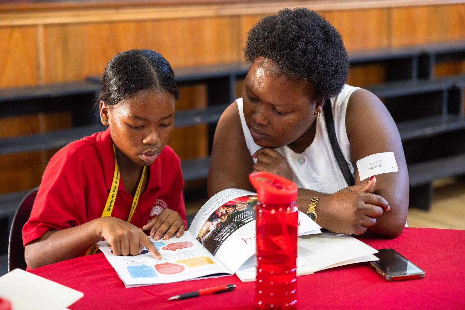 Students in red shirts work together at tables during an educational workshop or training session.