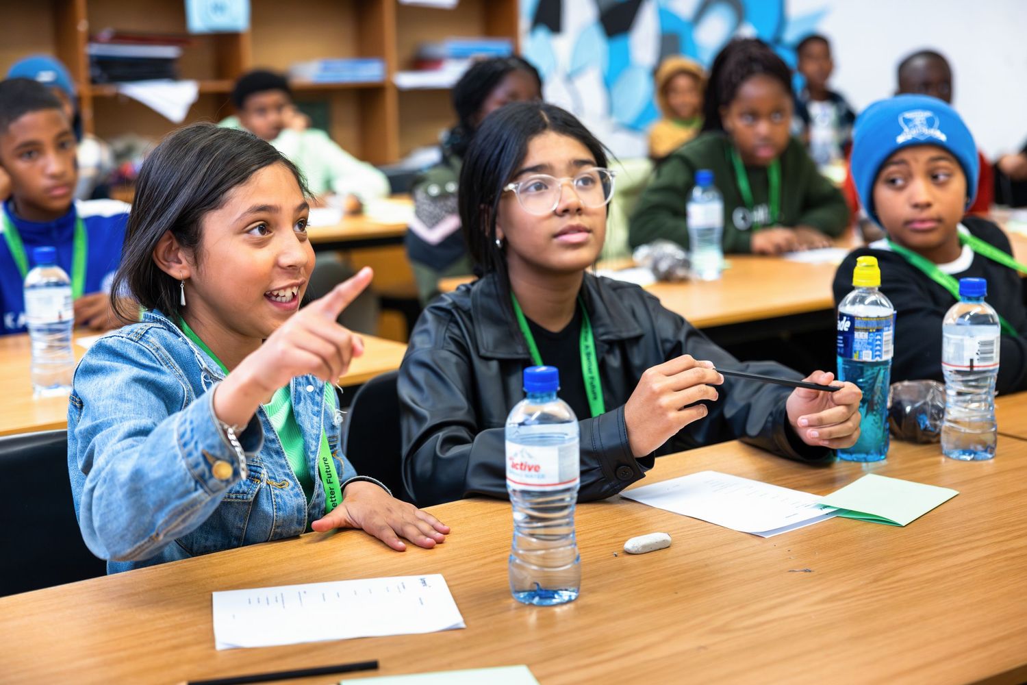 Students listening attentively during a classroom discussion with water bottles on their desks.