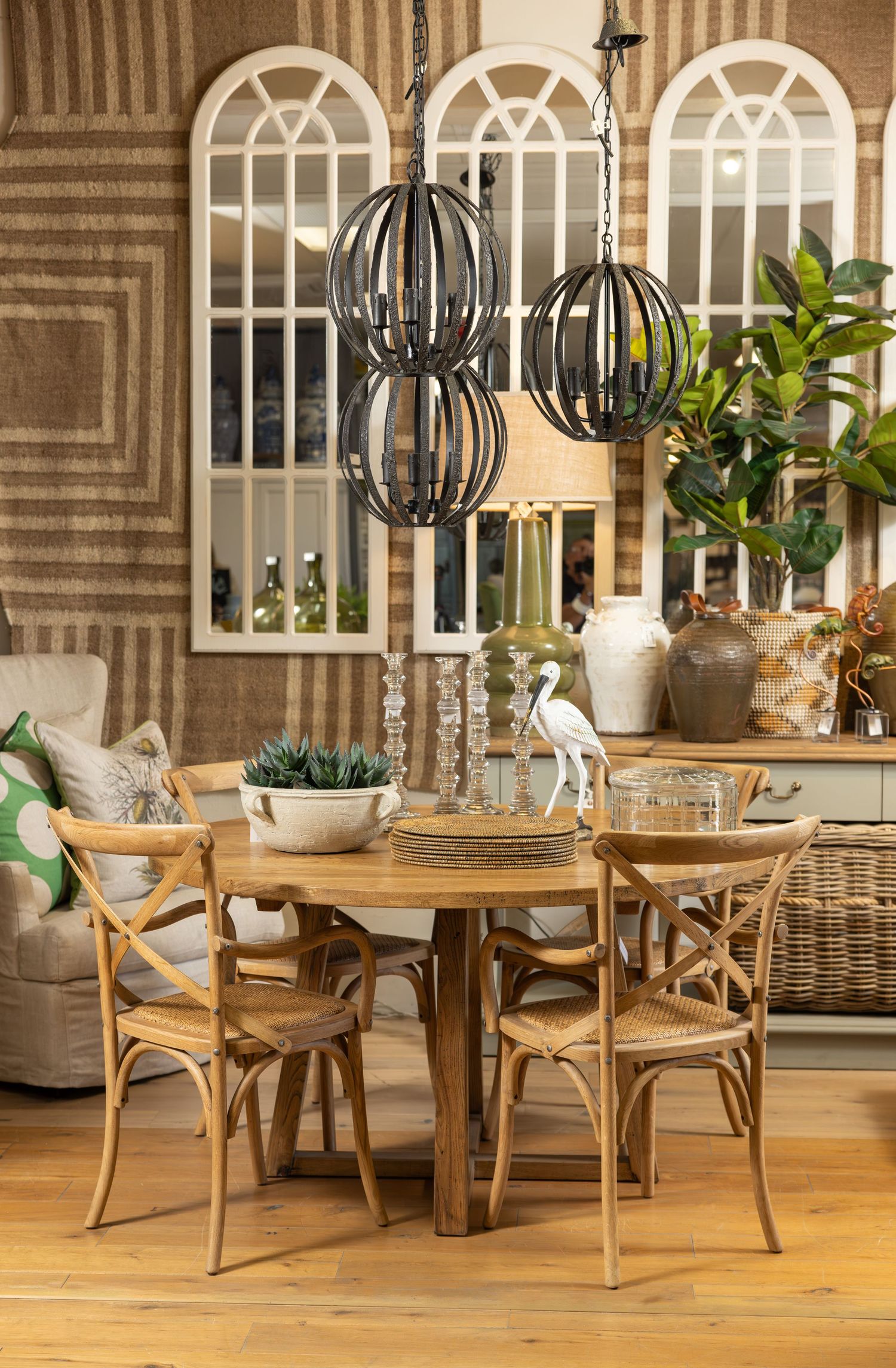 Dining area featuring round wooden table, cross-back chairs and arched window panels with sphere pendant lights.