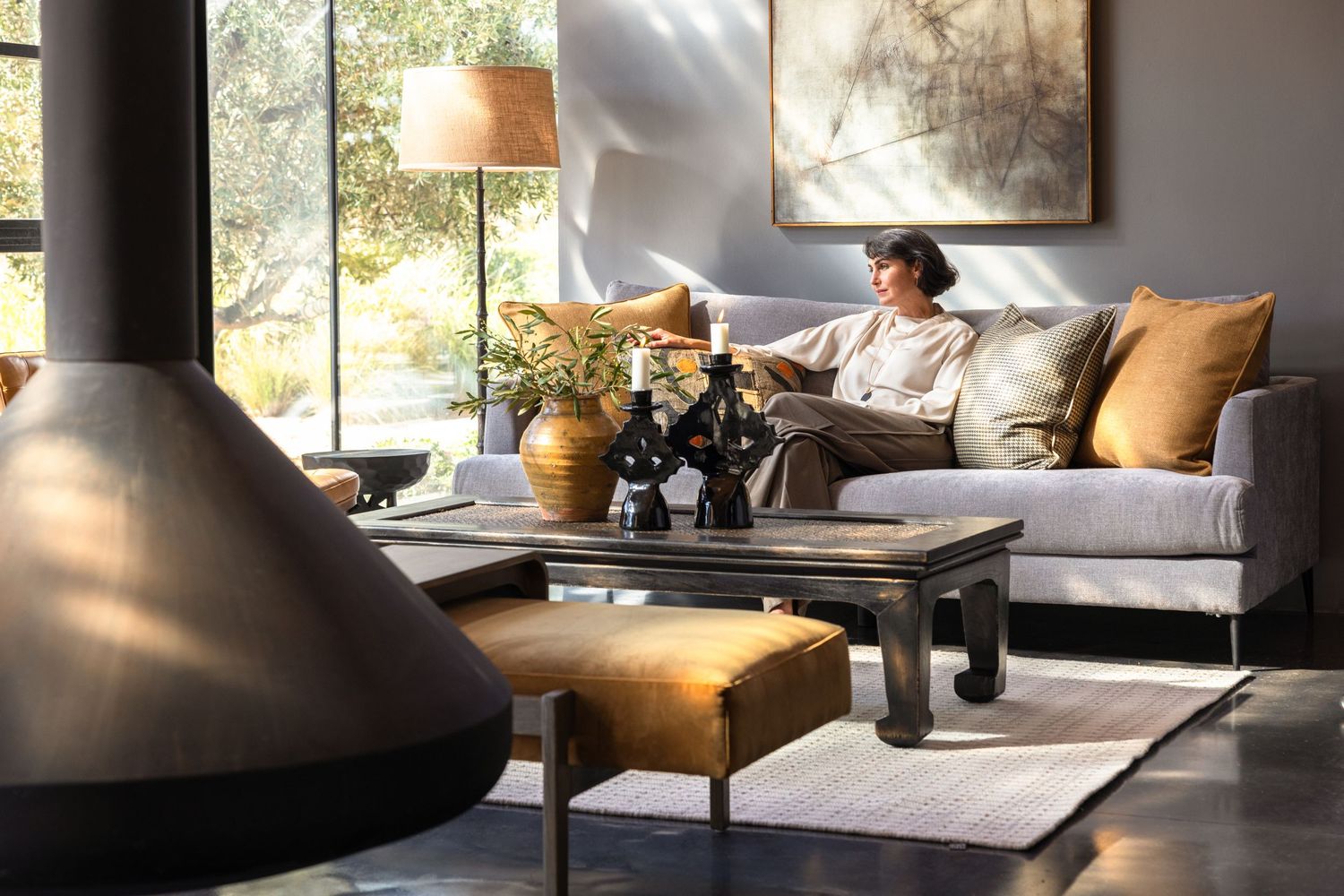 A cozy living room features a gray sofa, modern decor and large windows letting in natural light.