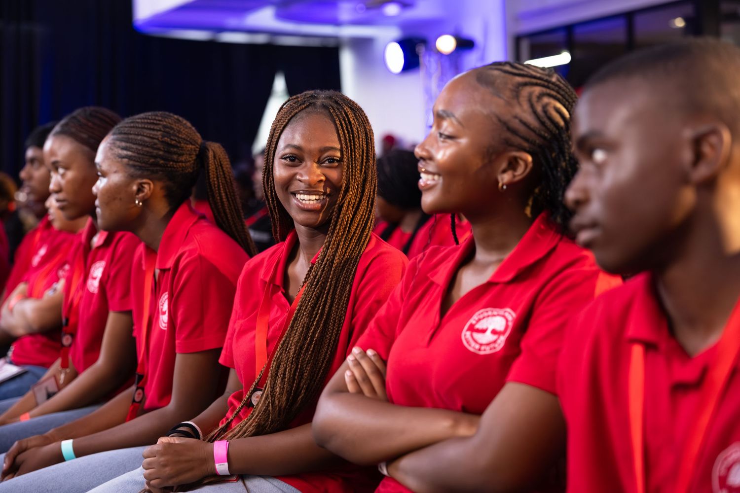 A row of students wearing matching red shirts sit together during an event with purple lighting.