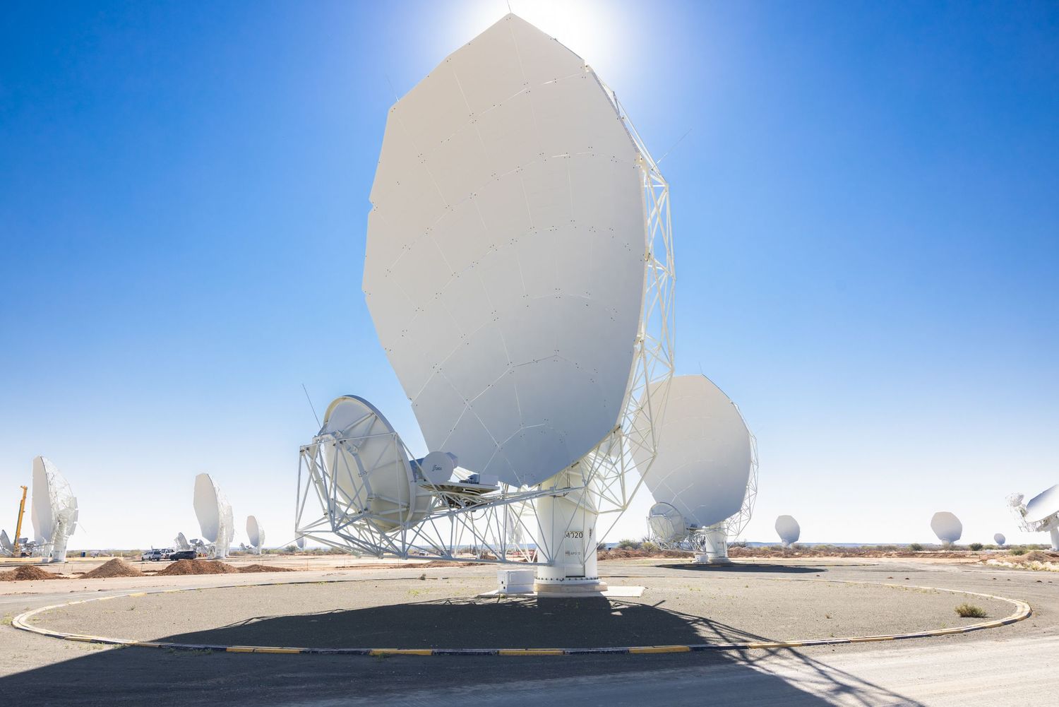 Large white satellite dish array with multiple receivers against blue sky background.