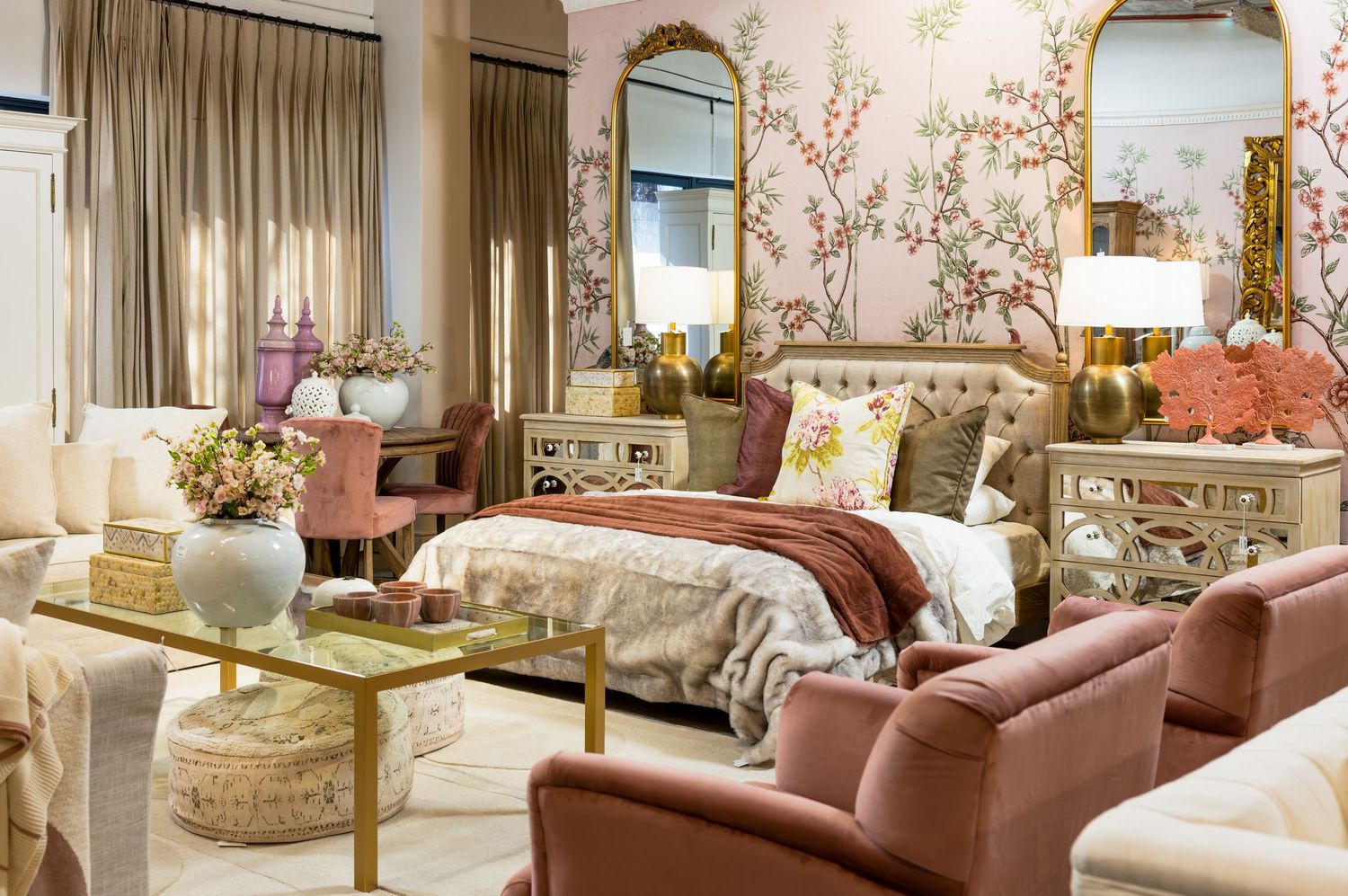 Romantic bedroom display with floral wallpaper, mirrored furniture, and soft pink chair accents.