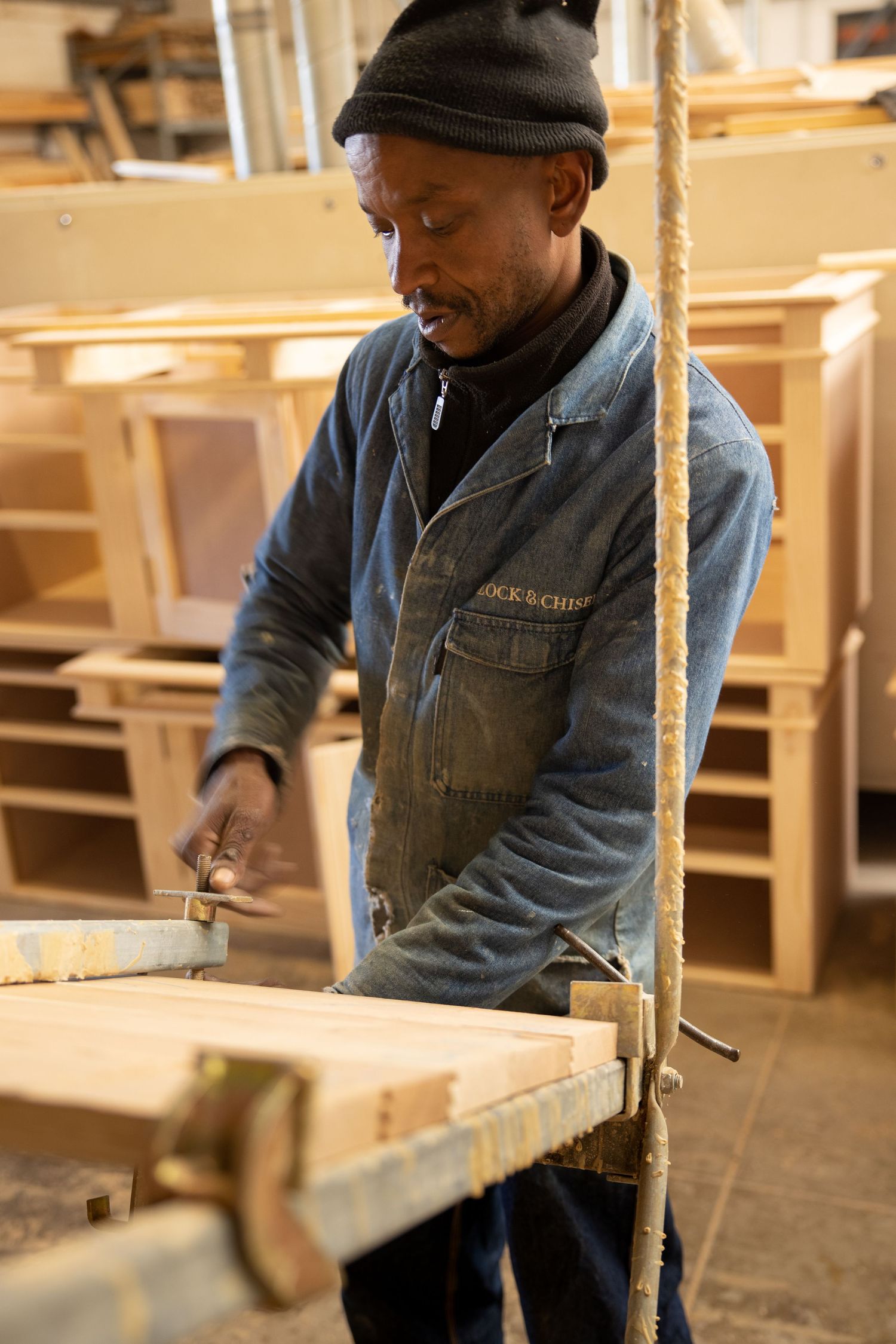 Worker in denim overalls focusing on detailed woodworking tasks.