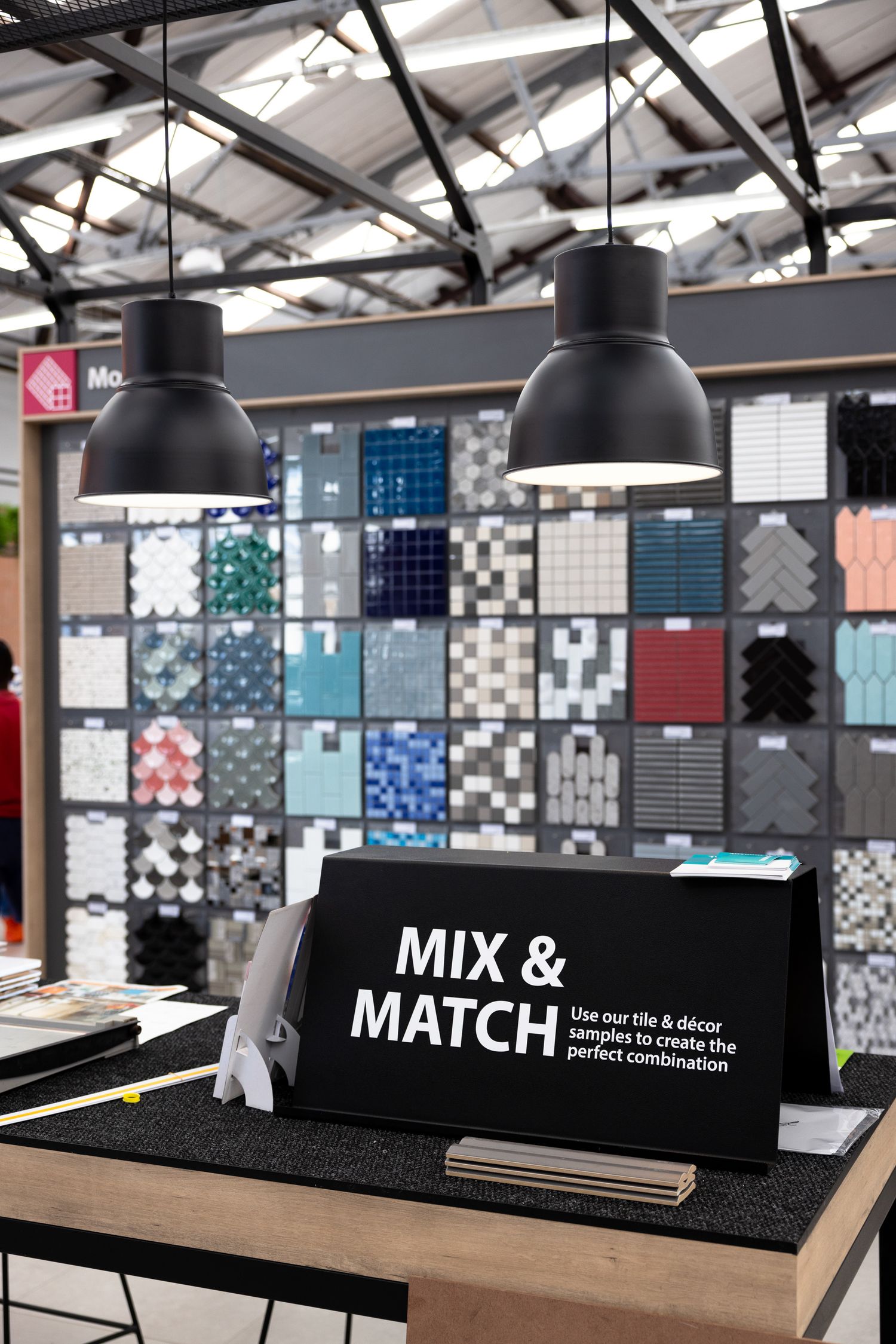 Showroom displaying various tile patterns with 'Mix & Match' signage under industrial pendant lights.