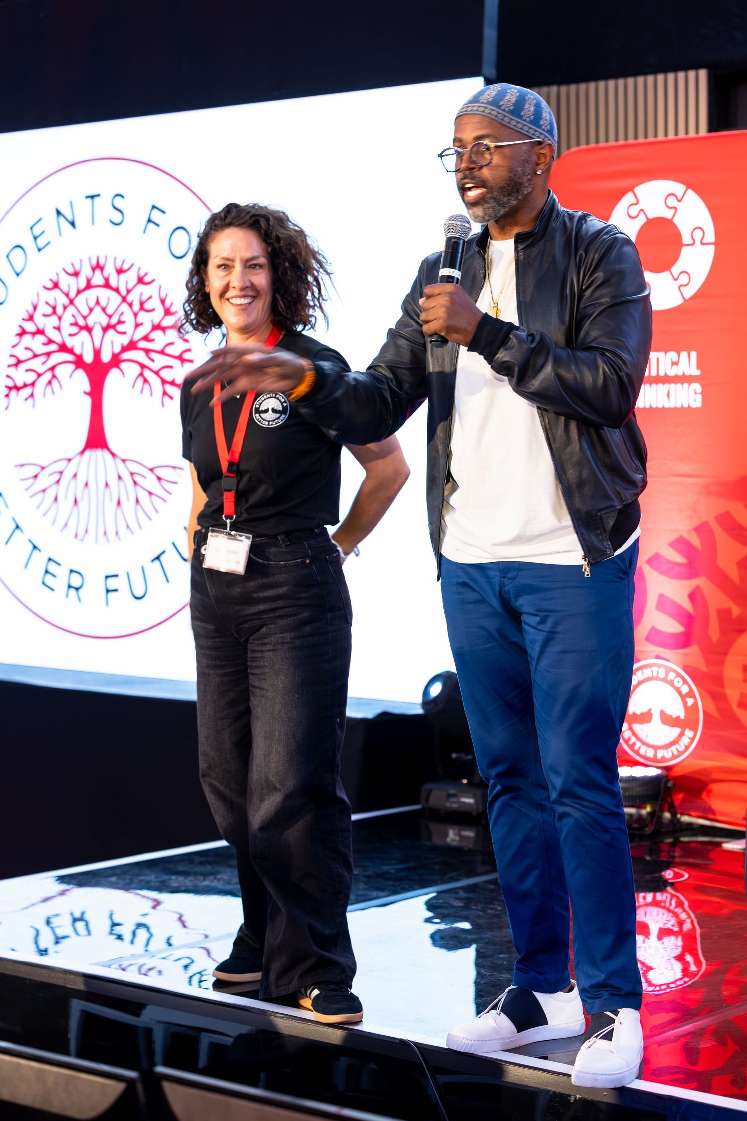 Two presenters share the stage at an educational conference with a tree logo displayed behind them.