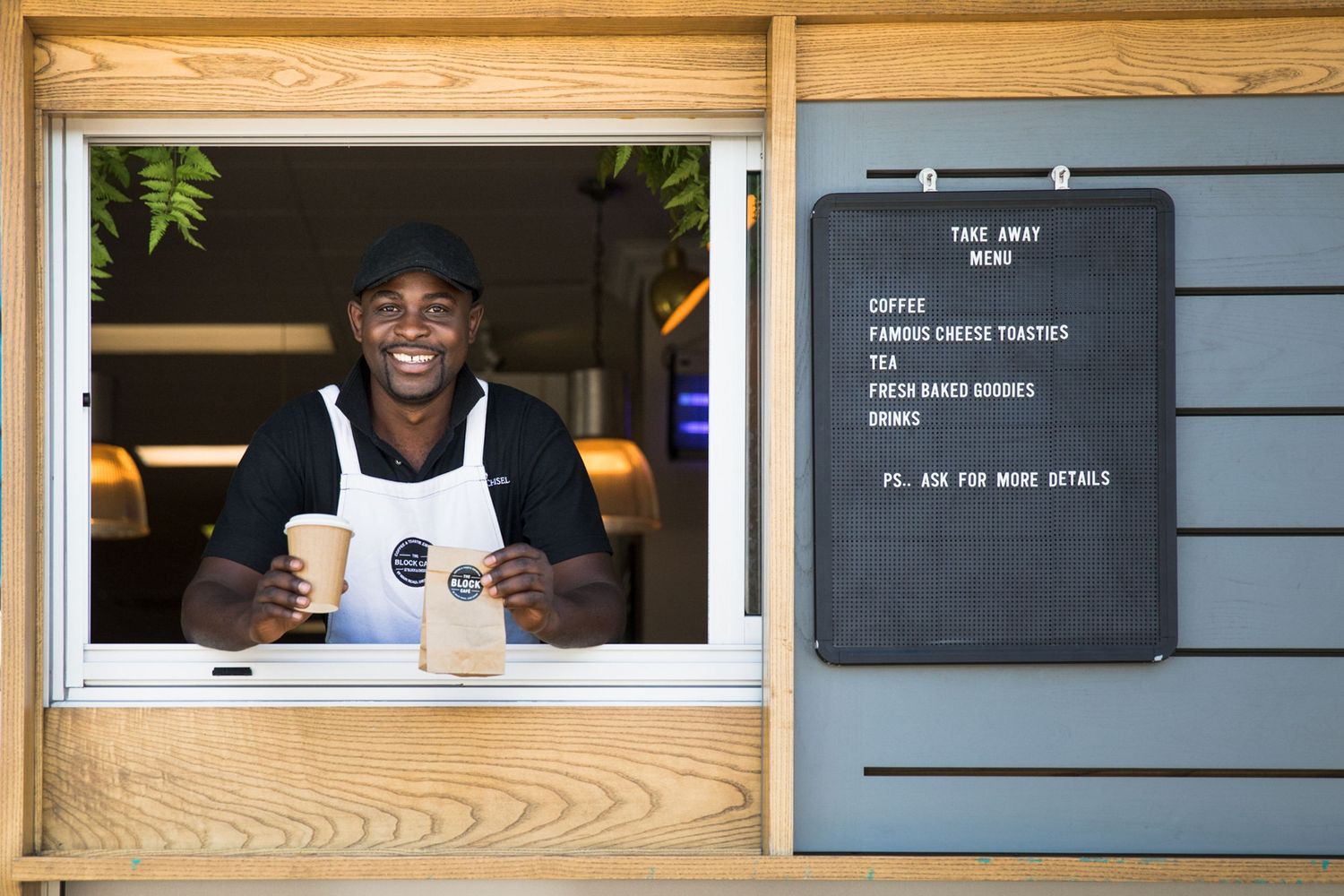 A modern coffee shop window counter with wooden panels and a smiling barista serving customers.