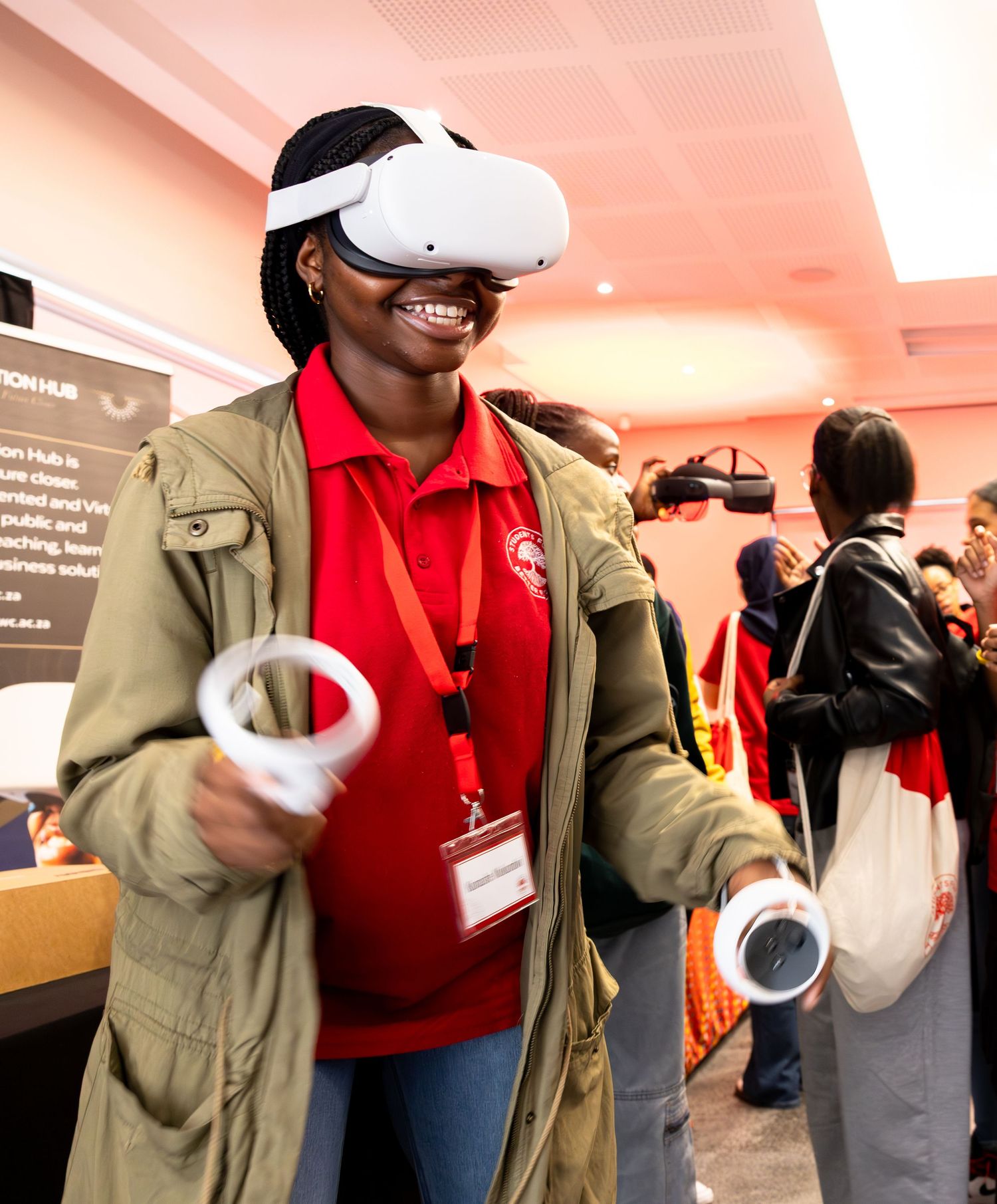 Students  wearing Meta Quest VR headset and holding controllers smiles while experiencing virtual reality at an event.