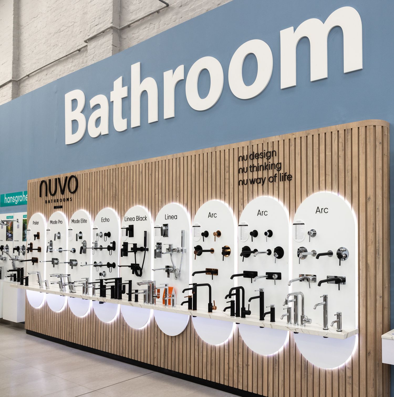 Long wall display of bathroom fixtures and faucets mounted on blue-tinted backdrop with wooden accents.