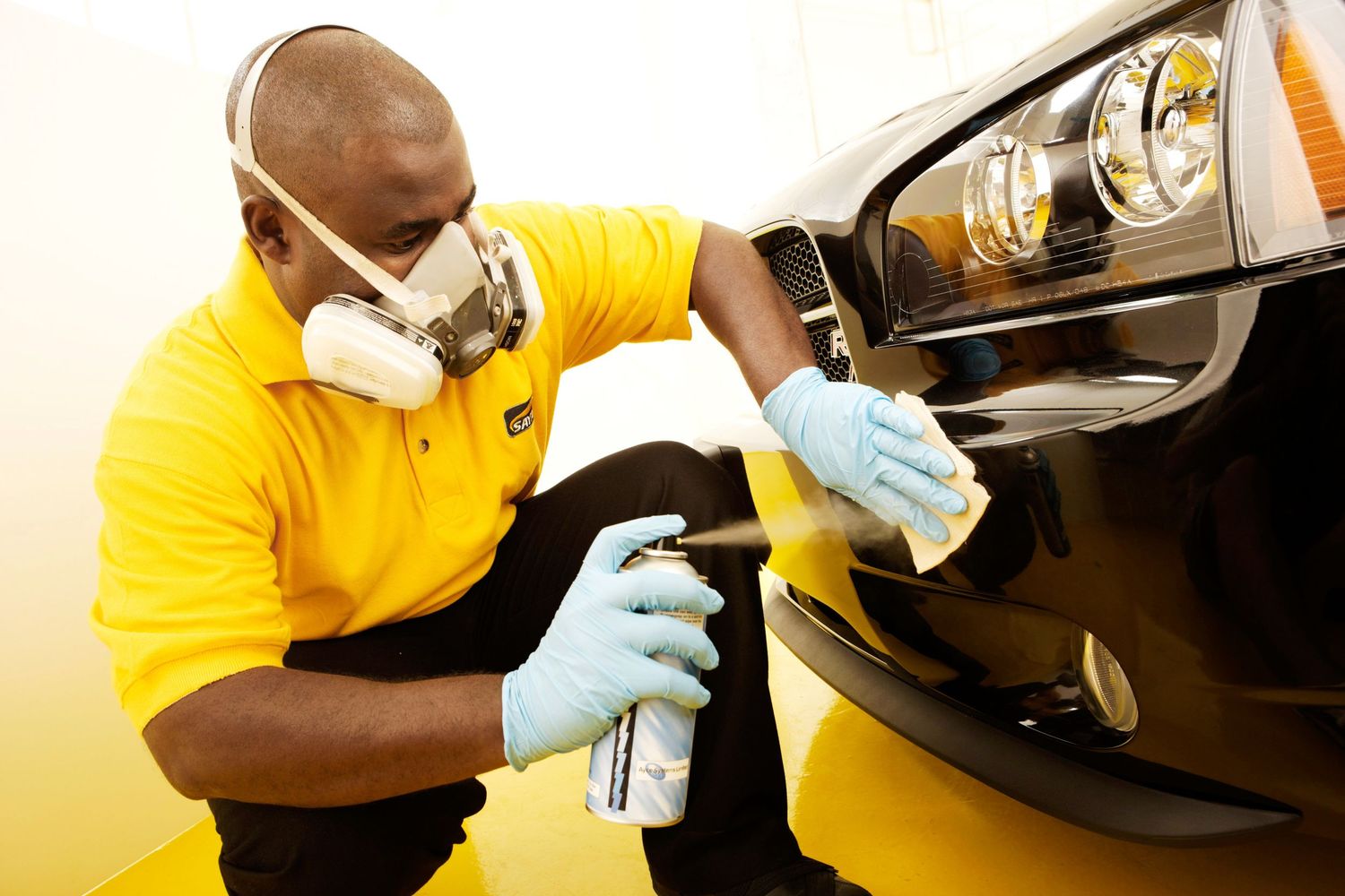 Auto technician in yellow uniform carefully inspects brake components of a vehicle during maintenance.