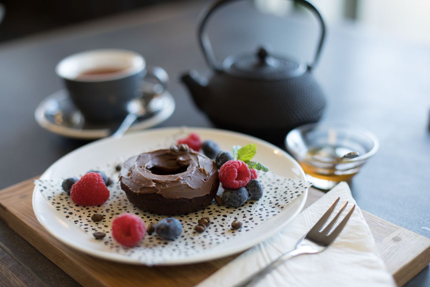 Chocolate dessert garnished with fresh raspberries on a white plate with decorative designs.