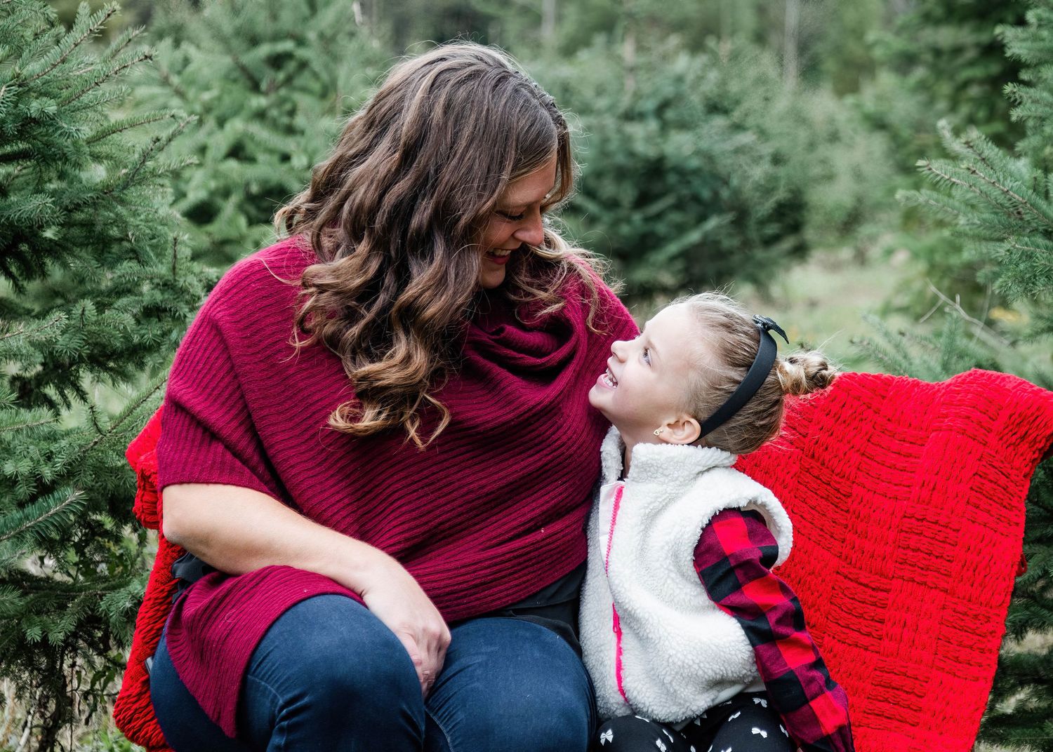 Family wearing burgundy and red sweaters poses together in a lush green forest setting.