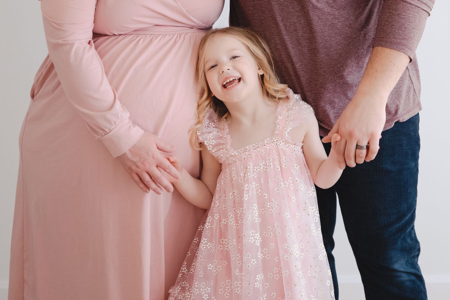 Family wearing coordinated pink outfits poses together in a studio setting for professional portraits.