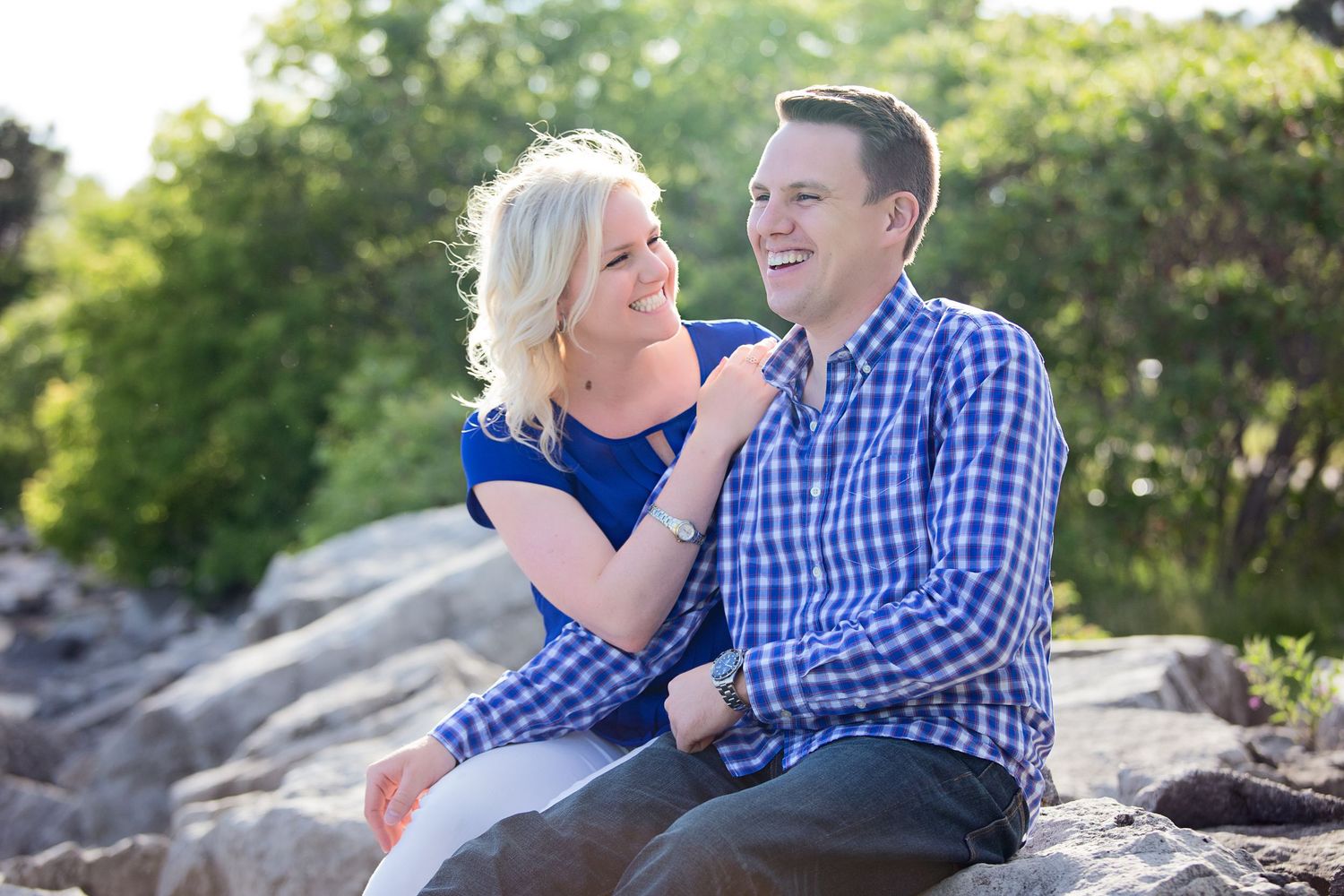 A couple sits together on rocky terrain, sharing a tender moment outdoors in natural lighting.