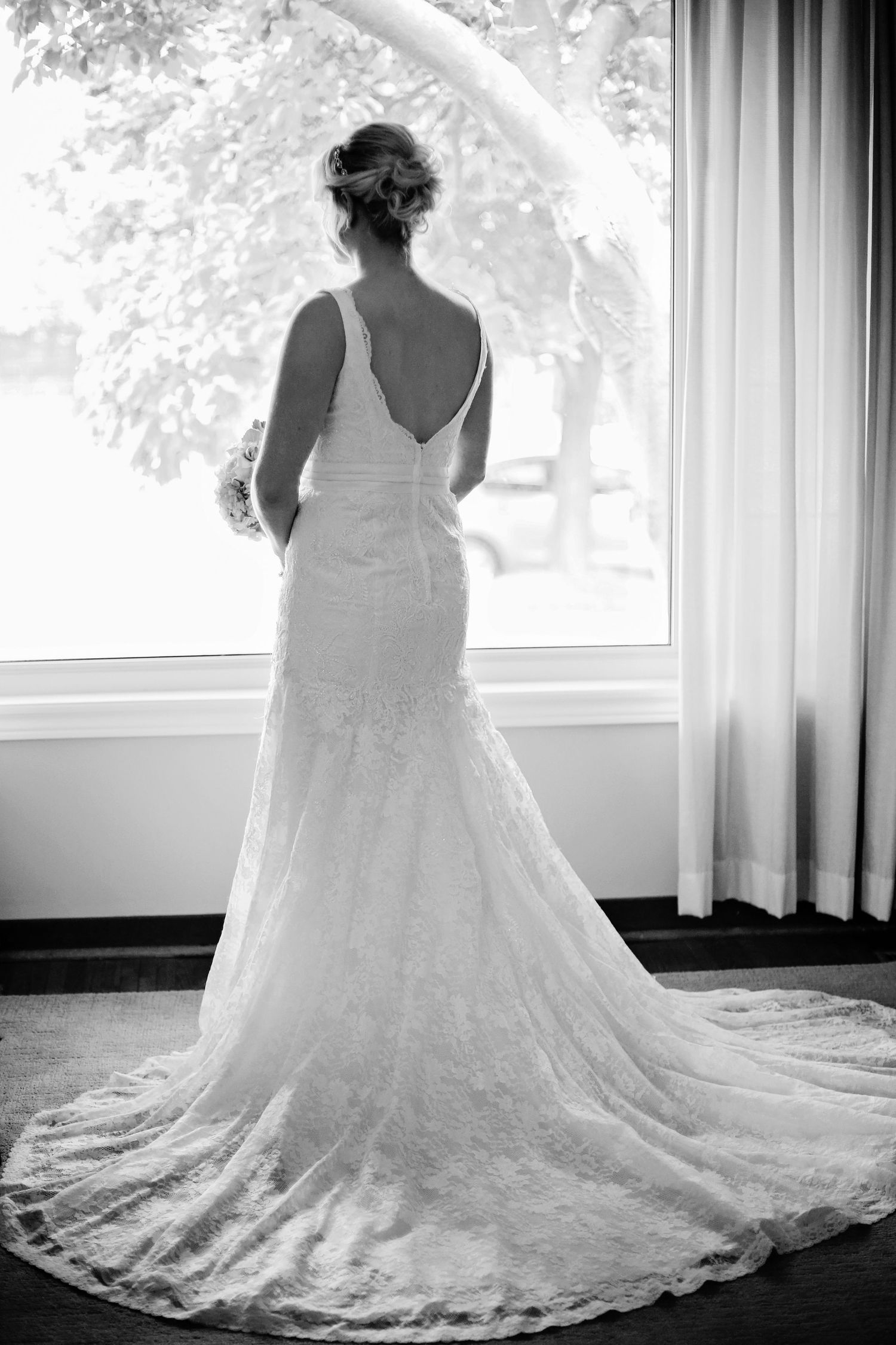 A black and white photo series showing the back and train details of a lace wedding dress near a window.