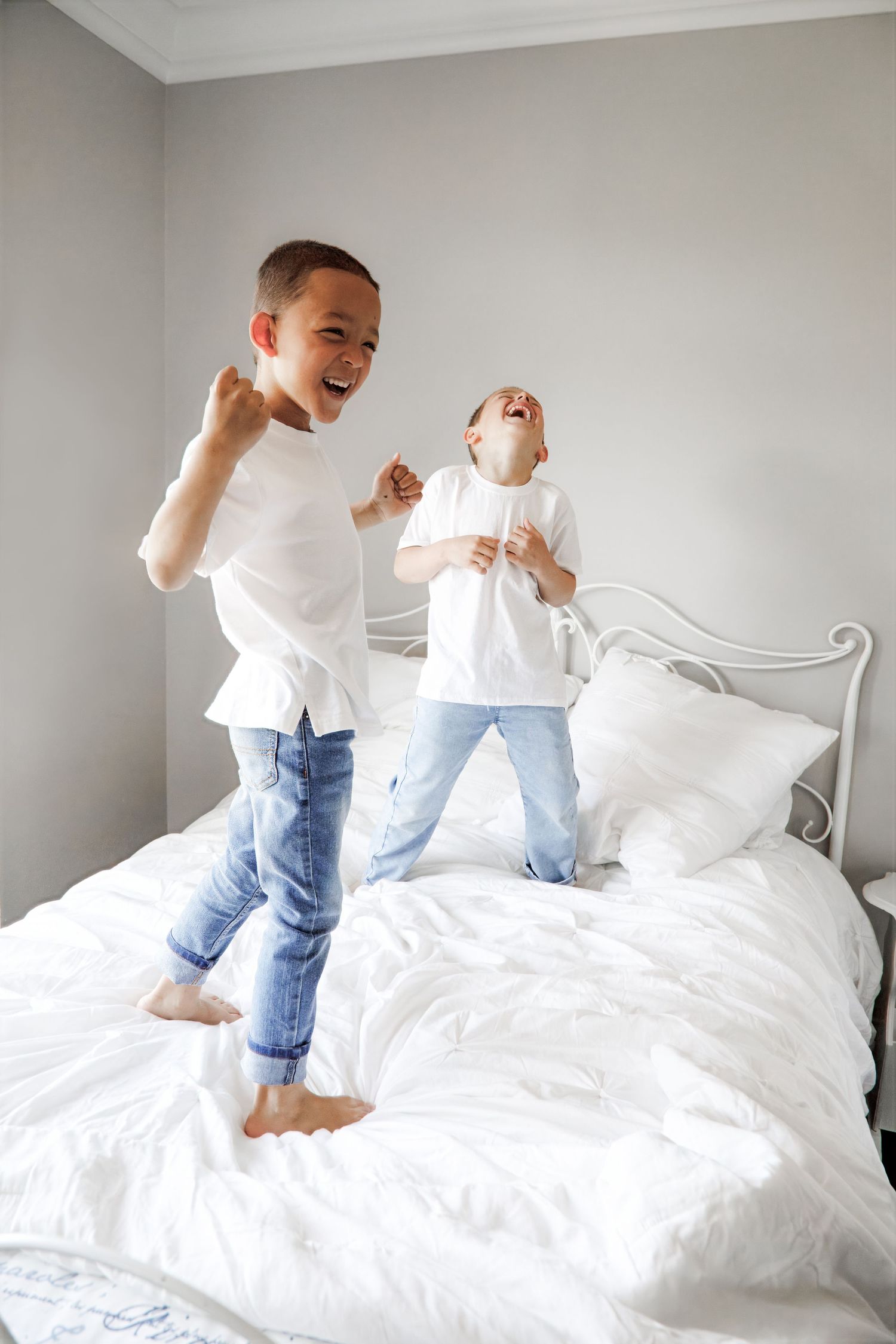 A sequence of playful moments shows two people in white tops and jeans jumping and playing on a white bed.