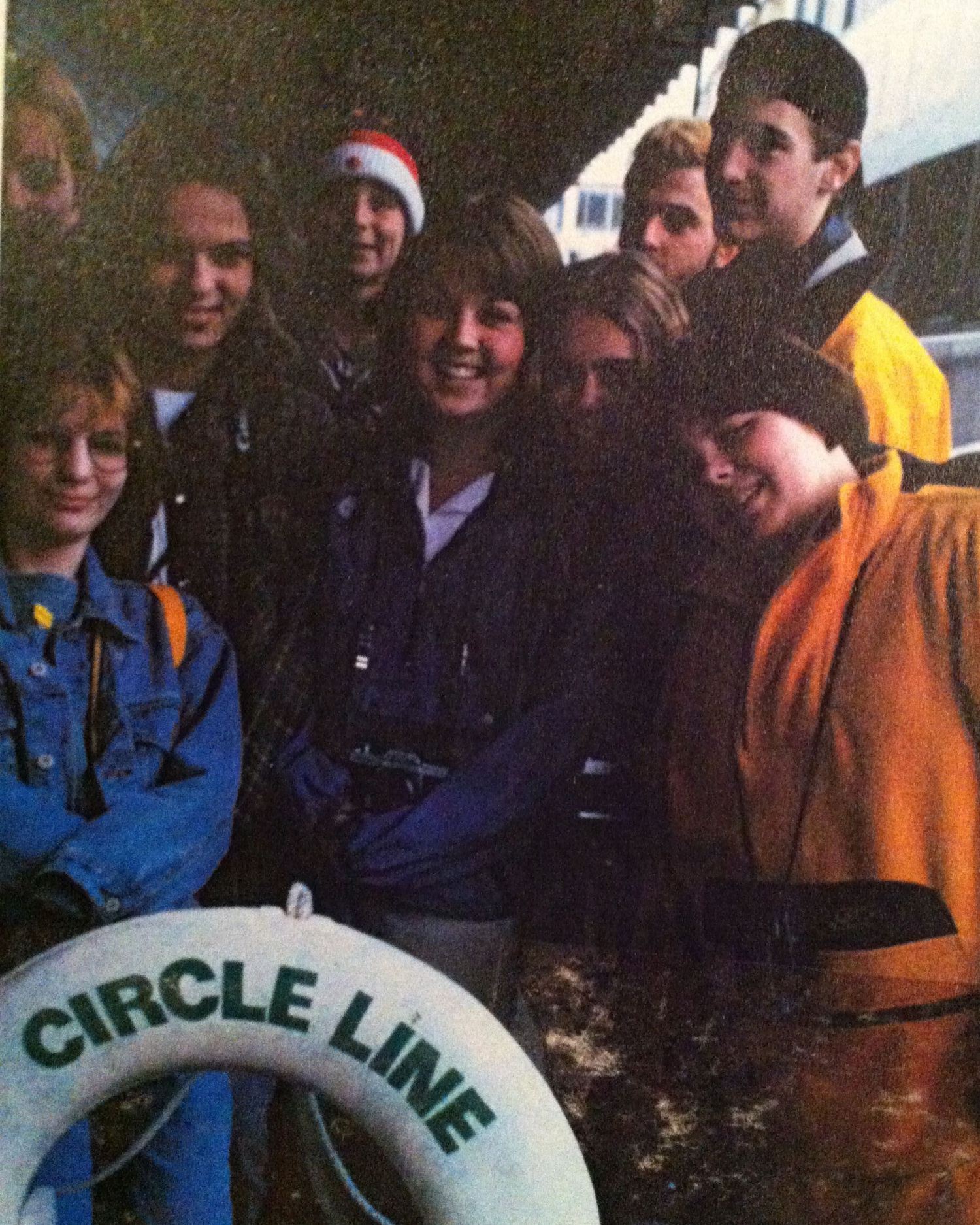 A group of students in blue uniforms and orange jackets gather together while smiling and interacting during an event.
