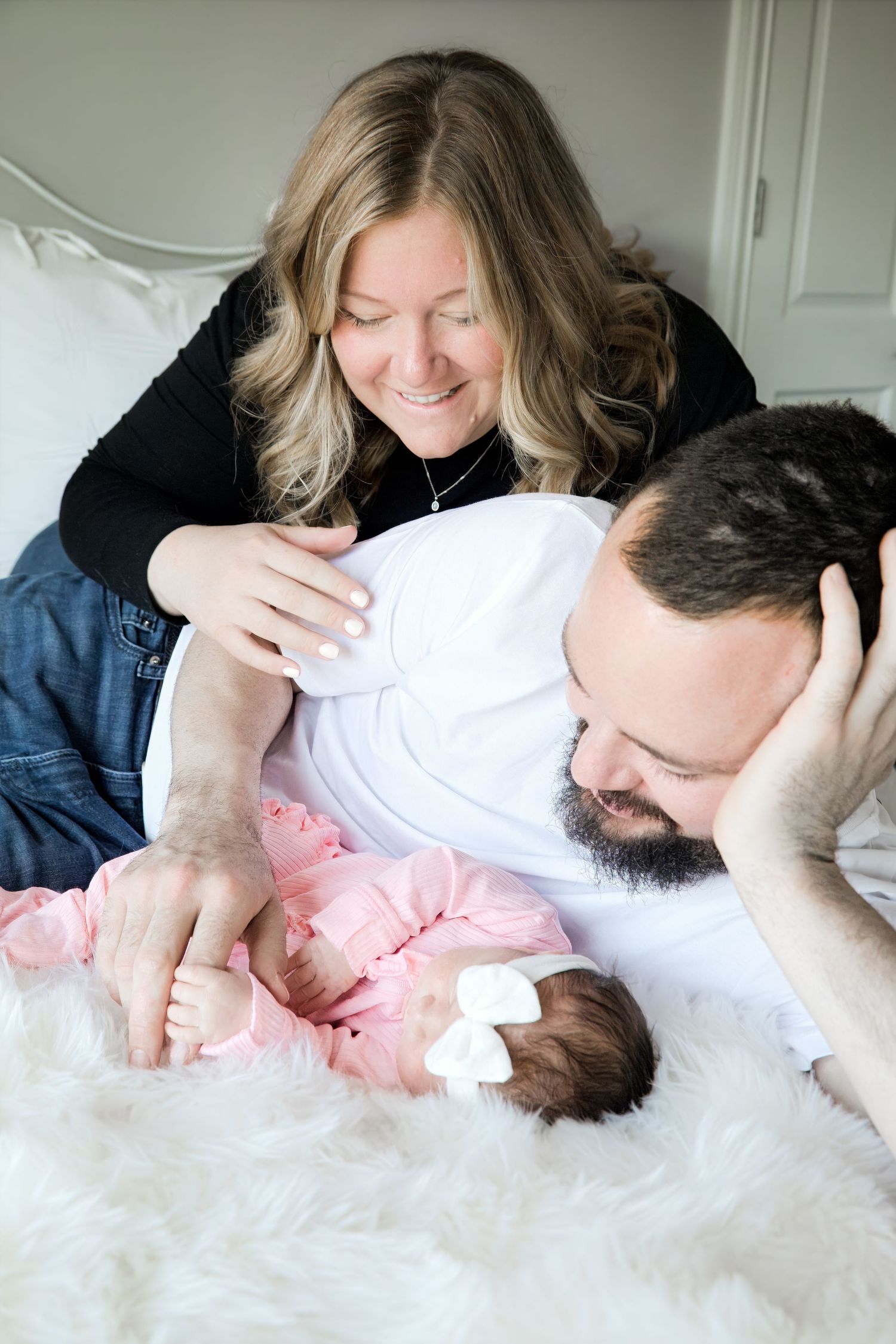 A series of intimate family photos showing tender moments with a newborn baby on white fur bedding.