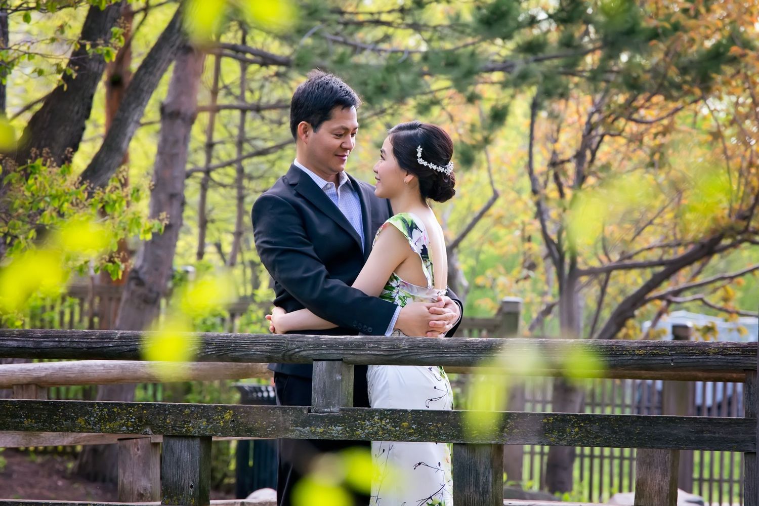 A couple shares a romantic moment on a wooden bridge in a lush garden setting during autumn.