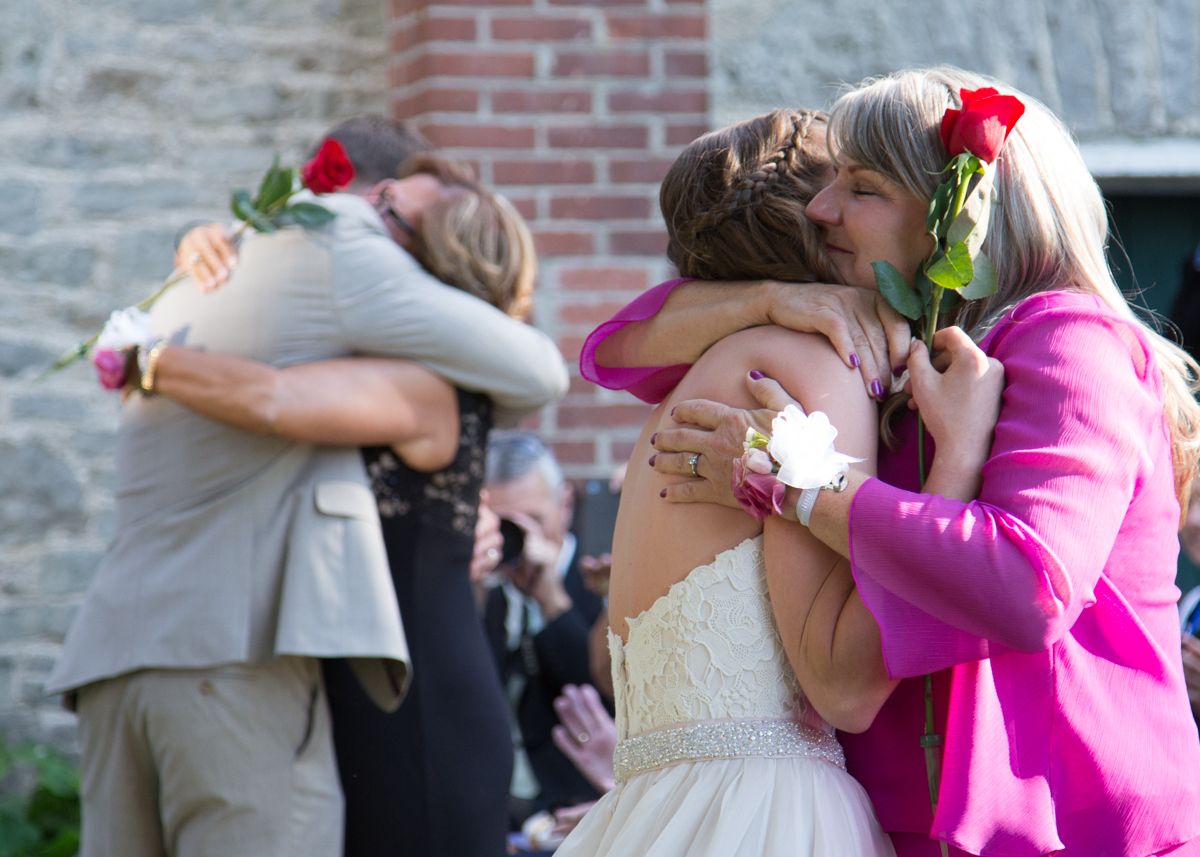 A sequence of wedding photos showing embraces between guests in pink and white formal attire against a brick wall.
