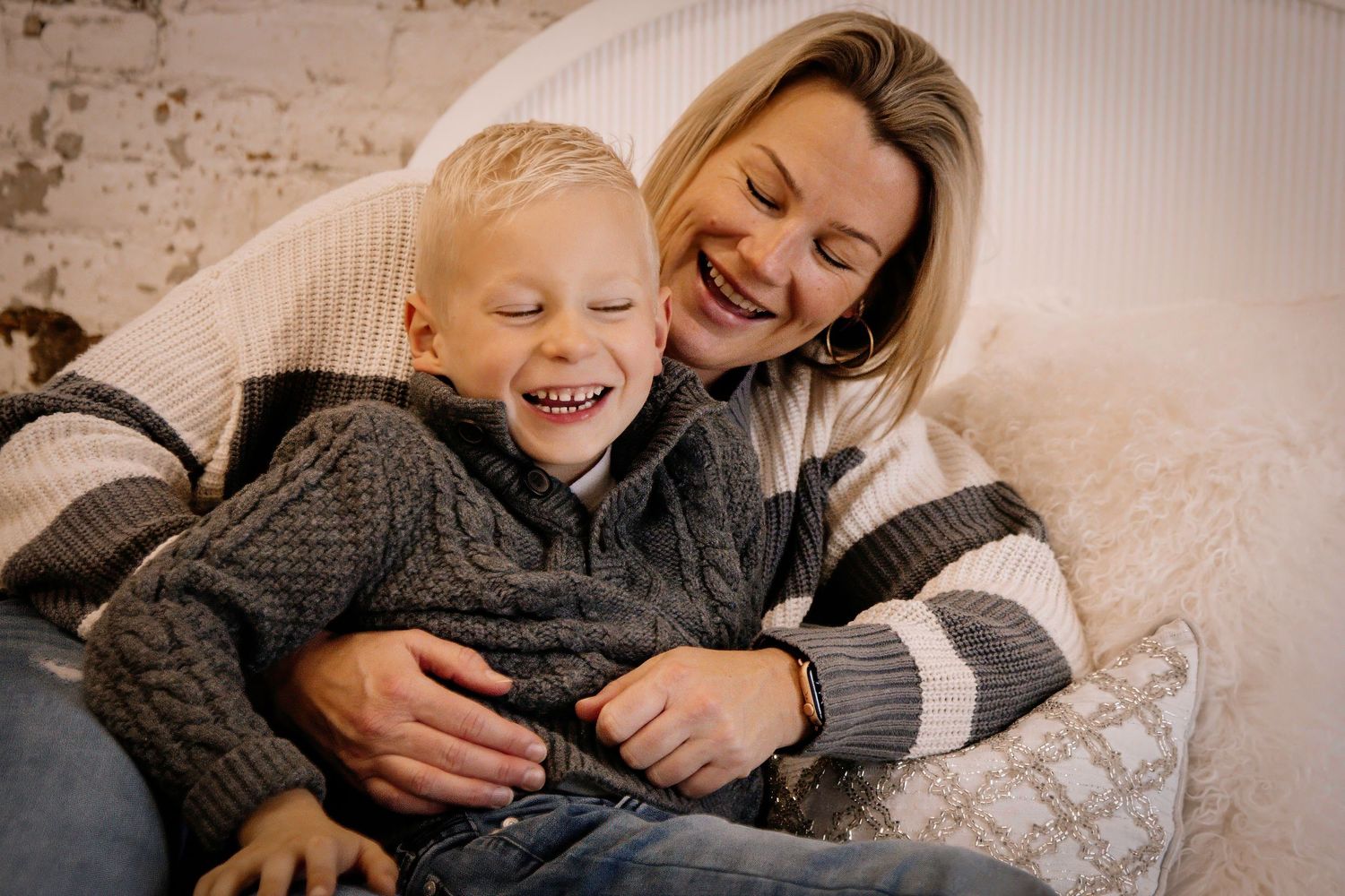 A parent and young child share a joyful moment while cuddling and laughing together on a couch.