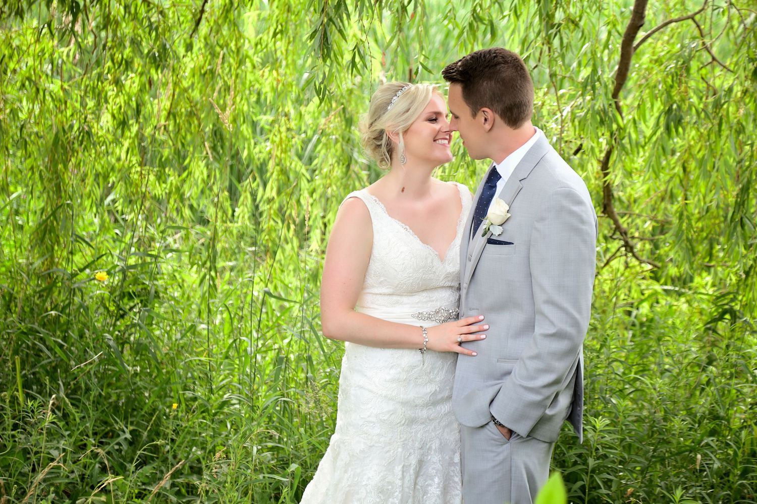 A bride and groom share a romantic moment under a weeping willow tree on their wedding day.