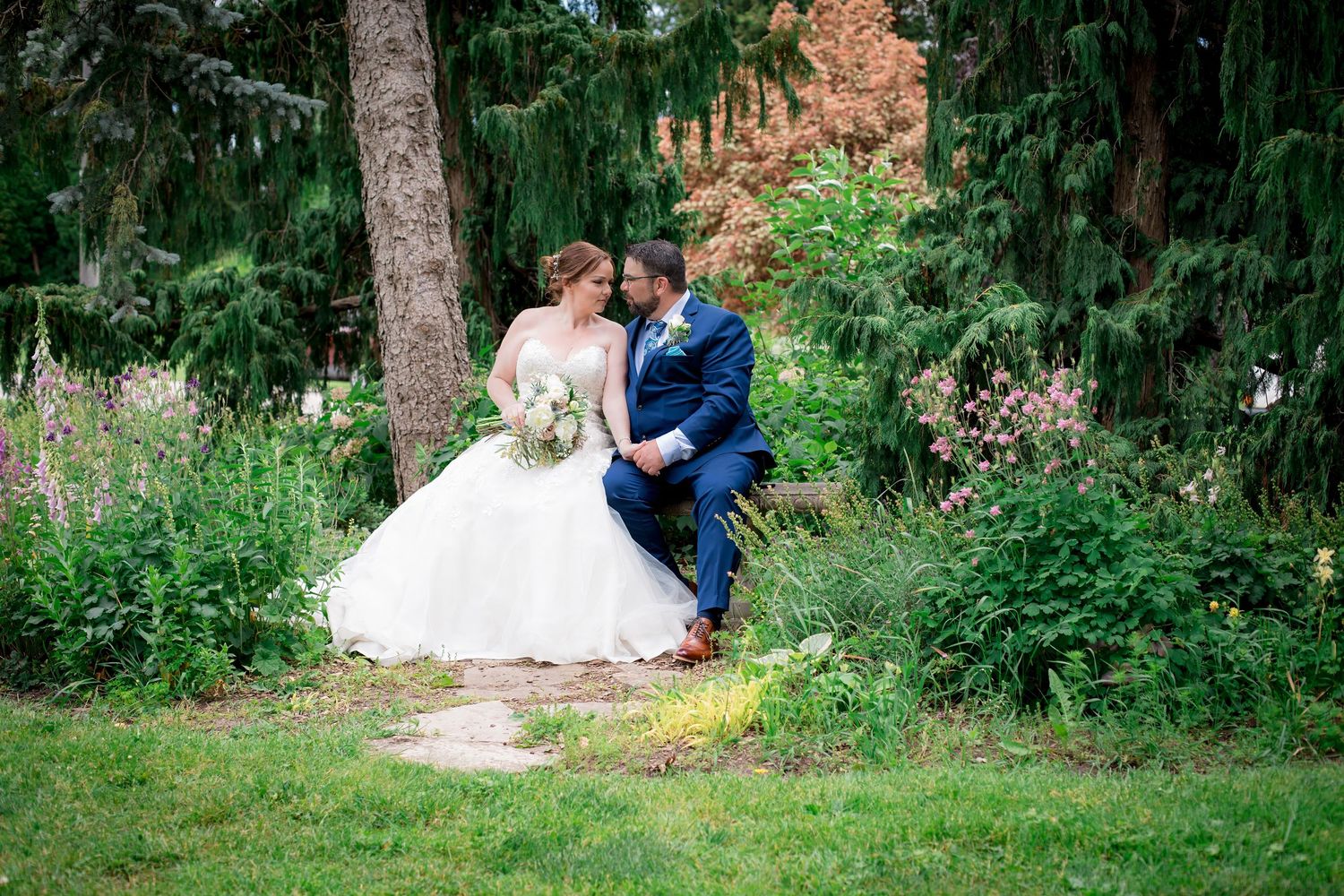 Romantic couple in formal attire share tender moments in a lush garden setting during their wedding photoshoot.