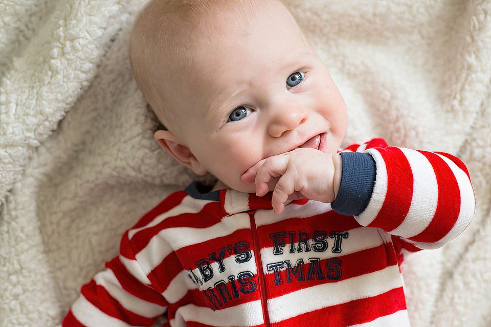Baby wearing red and white striped outfit smiles while lying on soft white blanket.