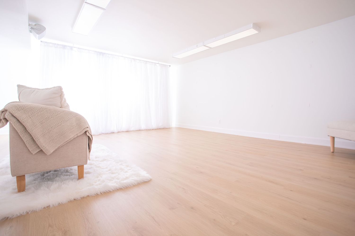 Modern minimalist living room interior with beige sofa and wooden flooring in natural light.