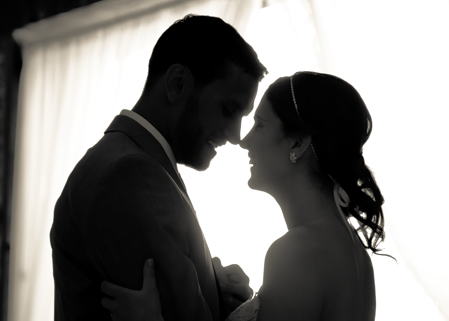 A romantic black and white silhouette of a couple sharing an intimate moment against a backlit window.