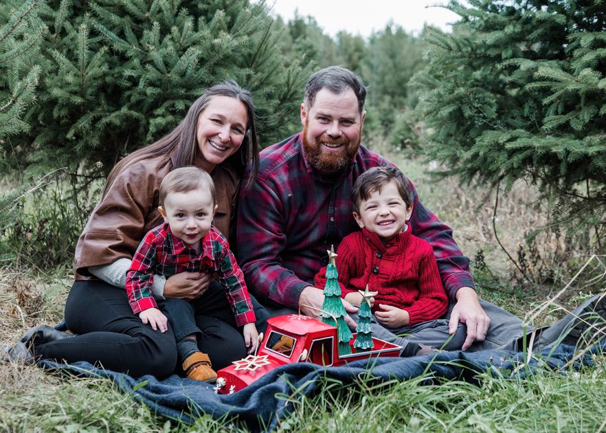 Family relaxes together on grass near evergreen trees during outdoor photo session.