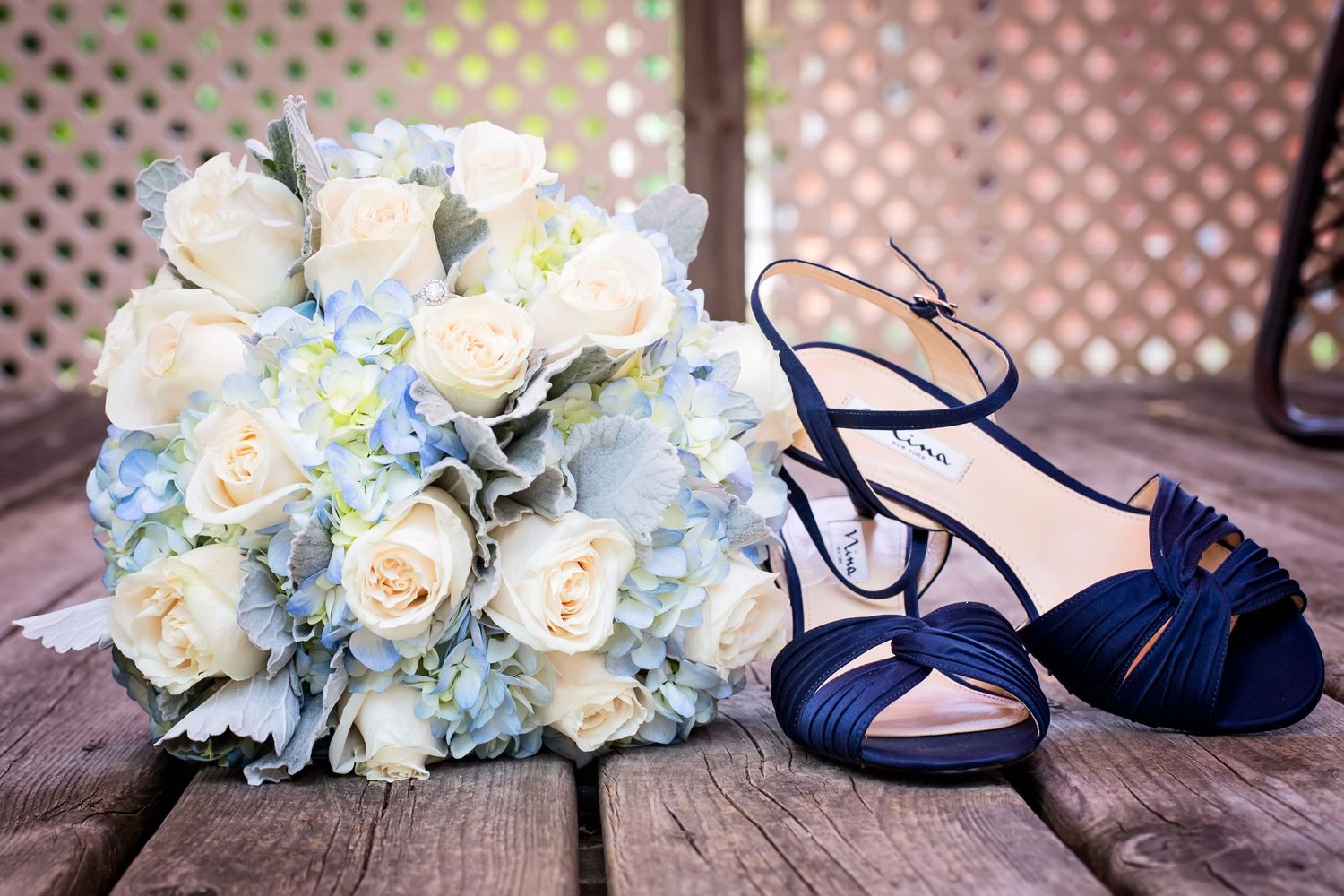 Navy blue wedding heels paired with a delicate white and blue floral bridal bouquet on rustic wooden surface.