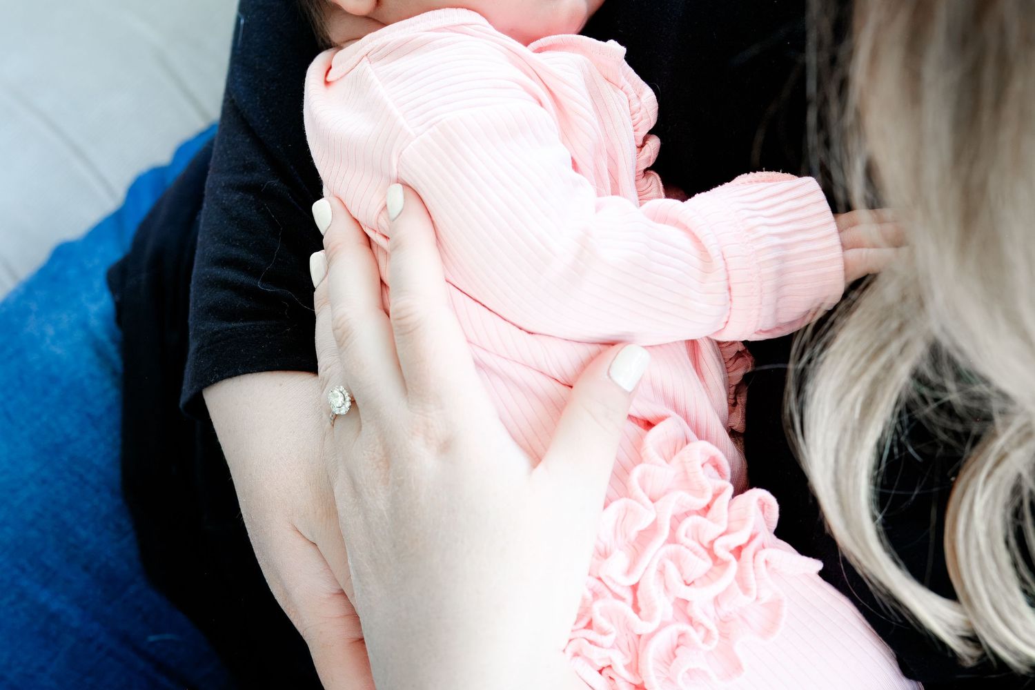A small baby wearing a soft pink knit outfit is being gently cradled in someone's arms.