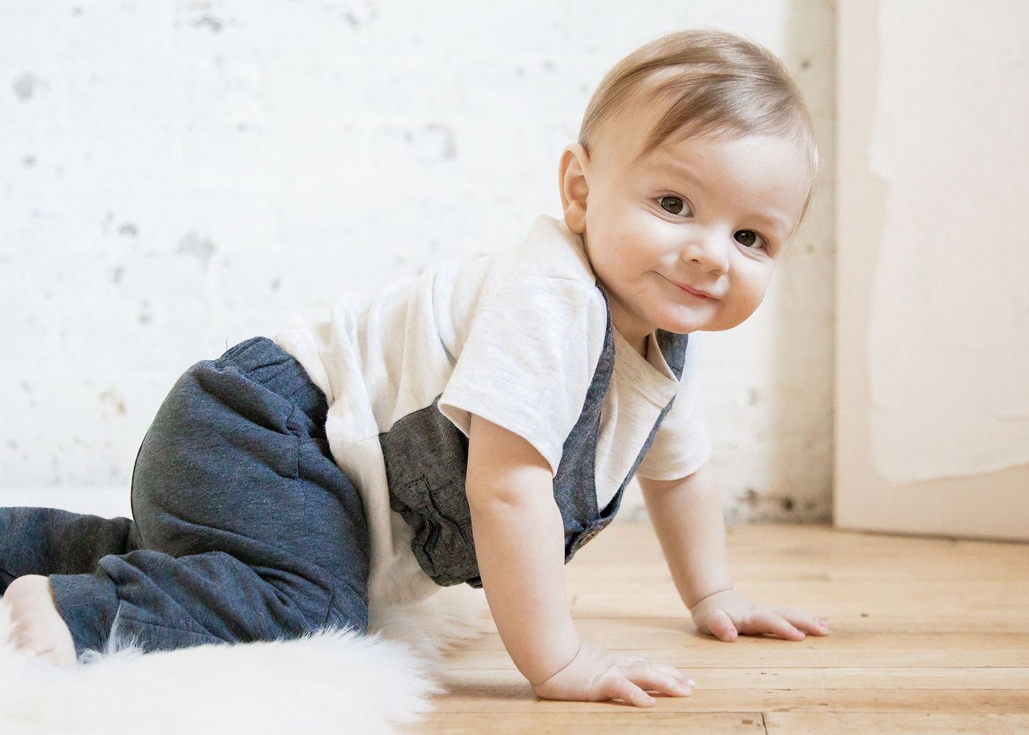 Baby crawling on wooden floor wearing navy pants and white shirt.