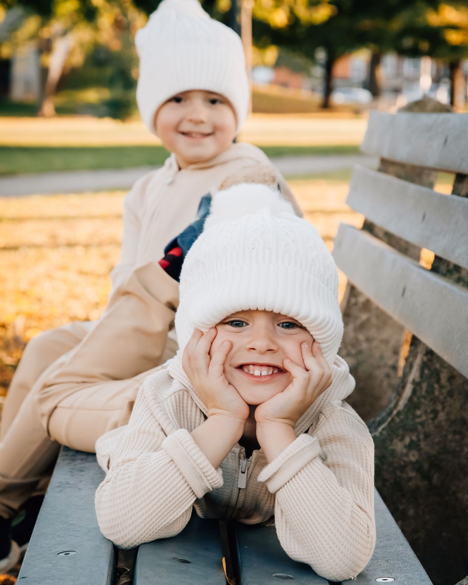 A child in a white knit hat playing playfully in autumn sunlight.